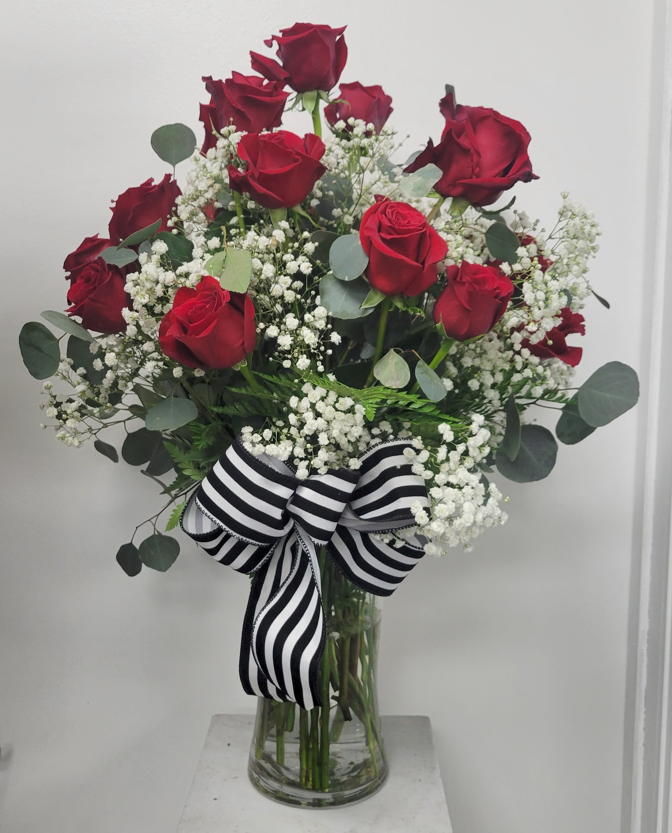 Red roses in a glass vase with white baby's breath and a striped ribbon