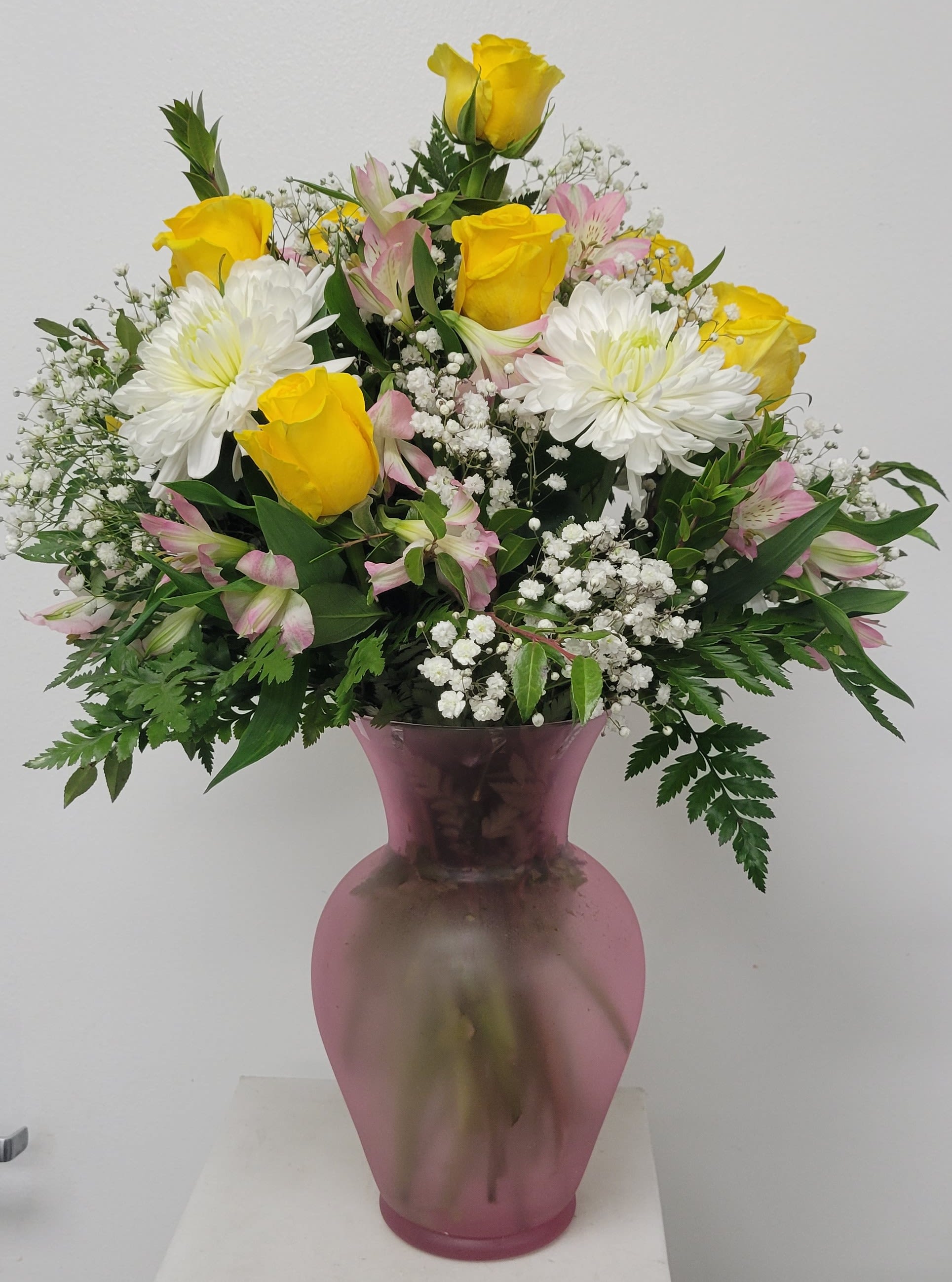 Yellow roses and white daisies in a pink vase