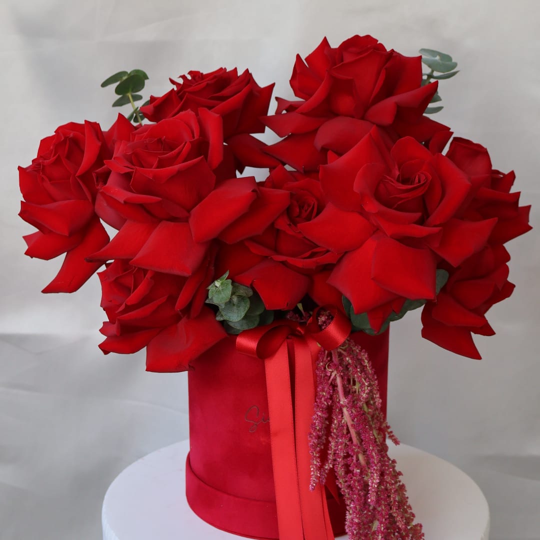 Red roses arranged in a red hat box with a ribbon and pink hanging filler