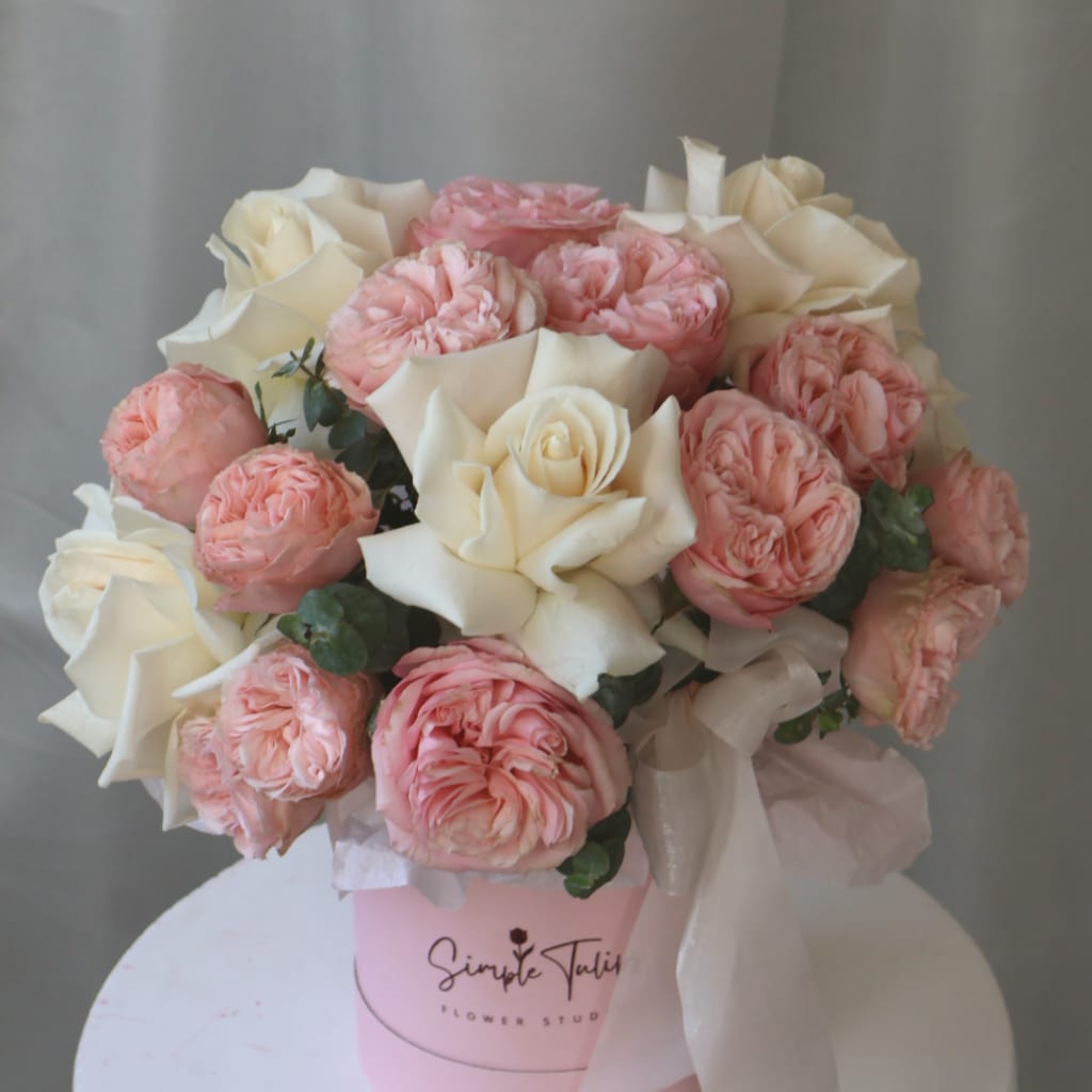 Pink and white roses arranged in a pink box with ribbon.