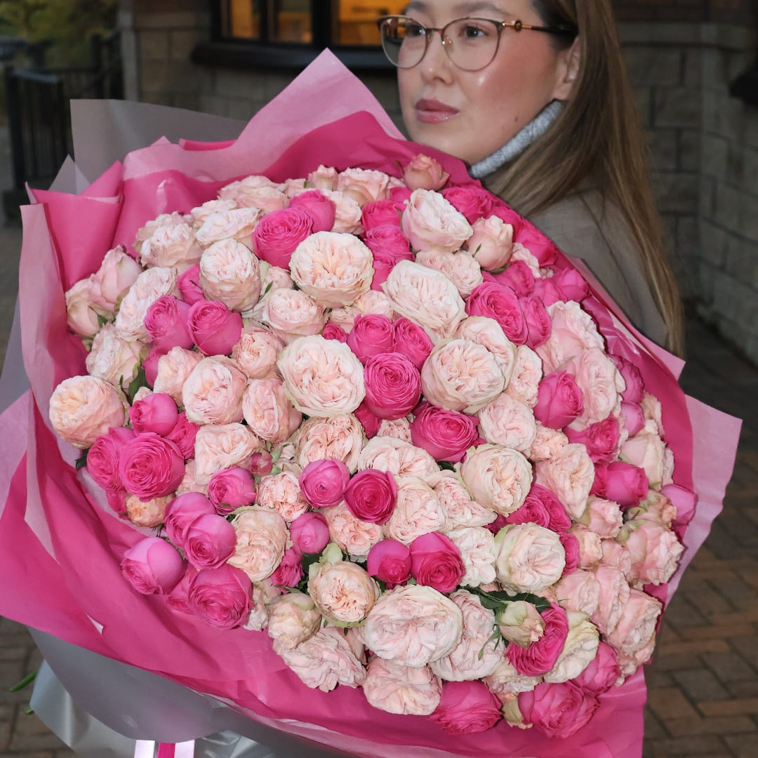 Woman holding a large bouquet of pink and blush roses wrapped in pink paper