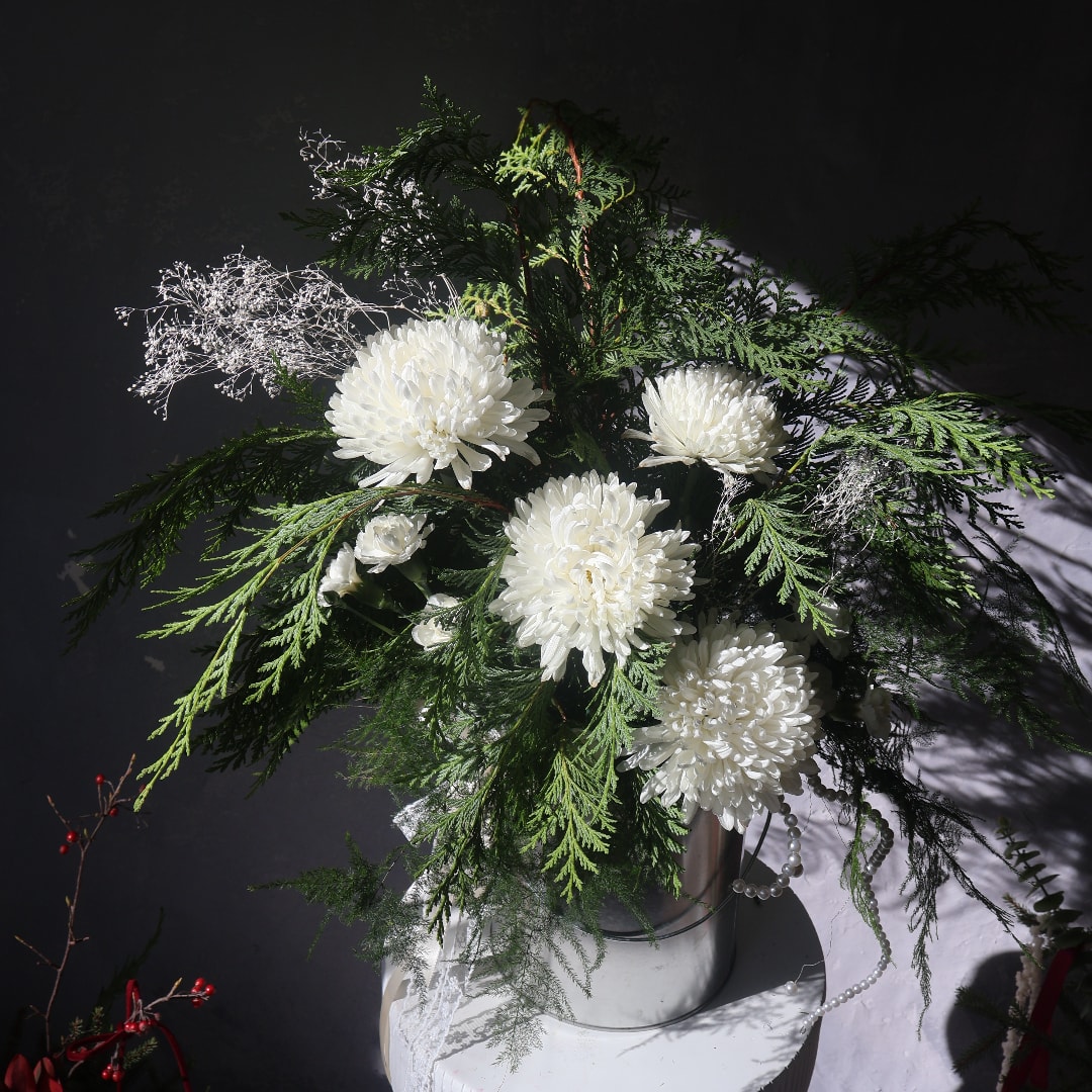 White chrysanthemum arrangement in a silver vase with evergreen foliage
