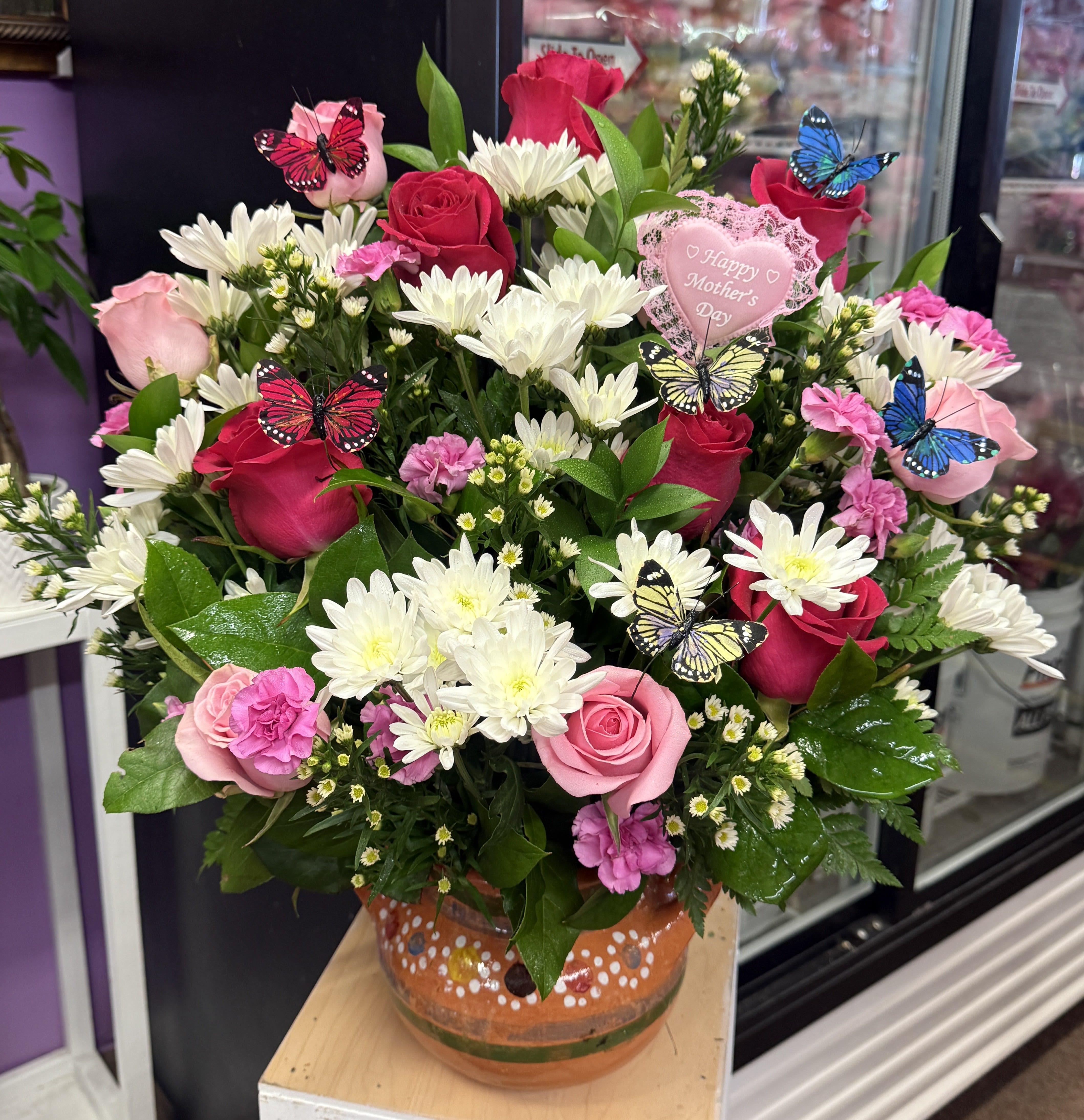 Pink and red rose bouquet with white daisies in a painted vase