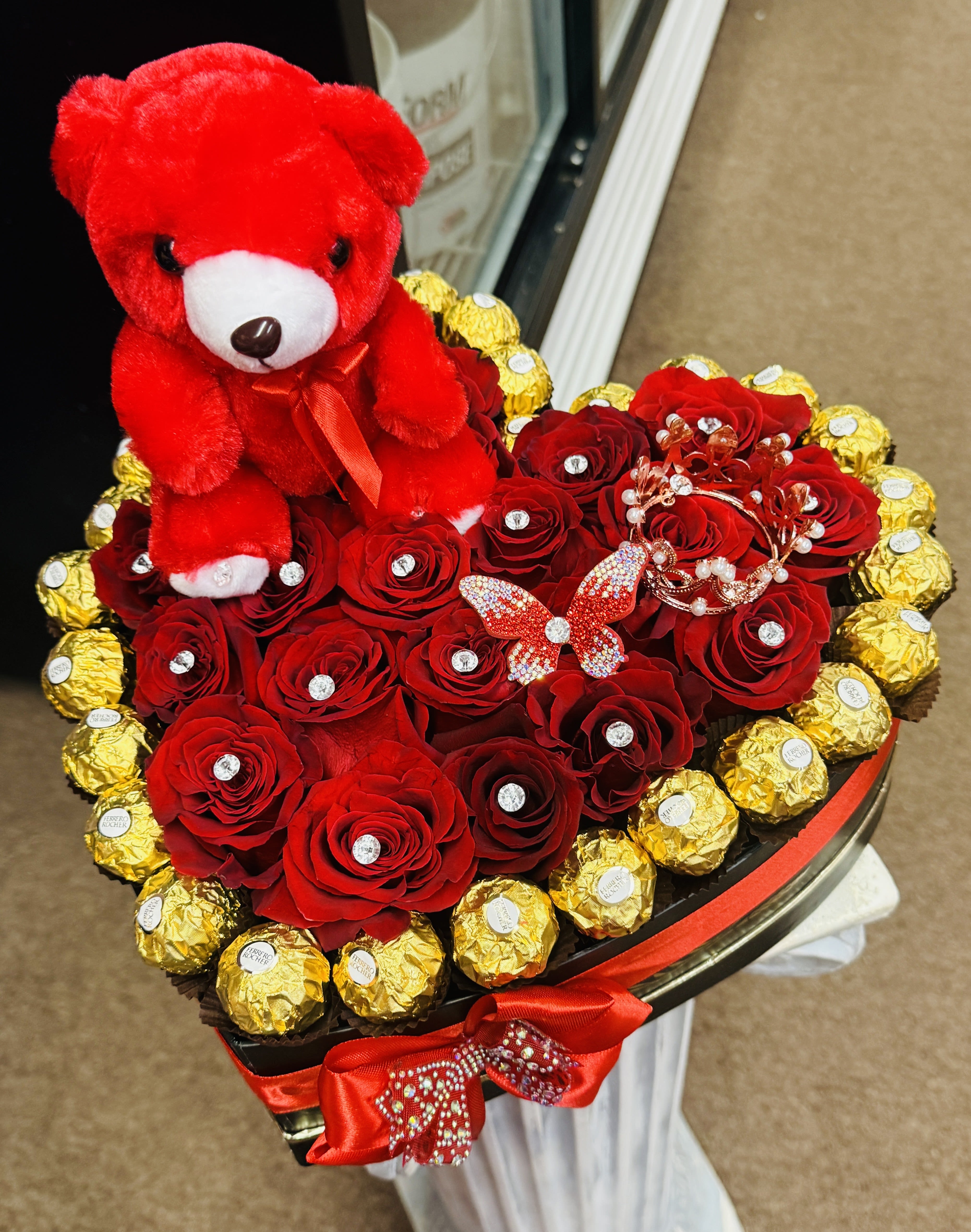 Heart-shaped bouquet of red roses with a red teddy bear and gold-wrapped chocolates
