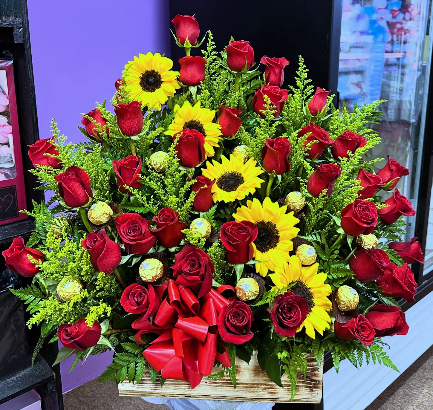 Large bouquet of red roses and yellow sunflowers in a wooden box with a red bow