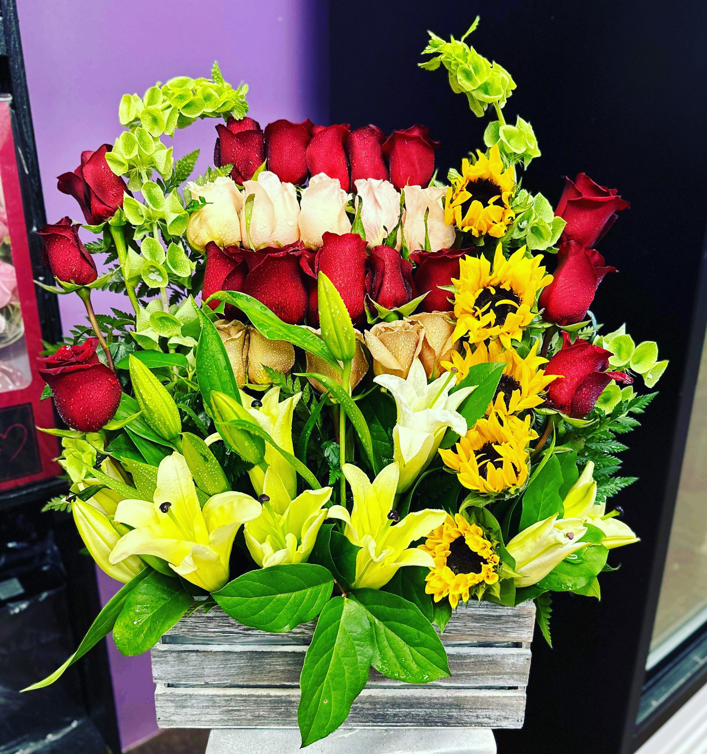 Mixed bouquet of red and cream roses with yellow lilies in a wooden box