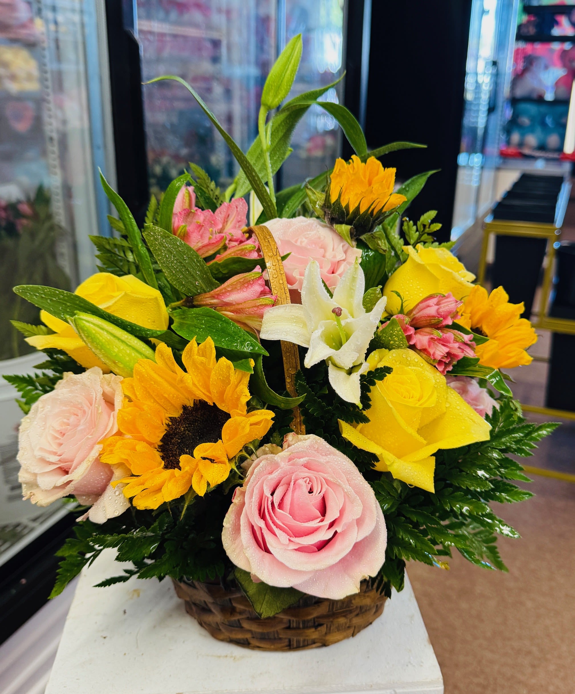 Basket arrangement of pink and yellow roses with sunflowers and white lilies