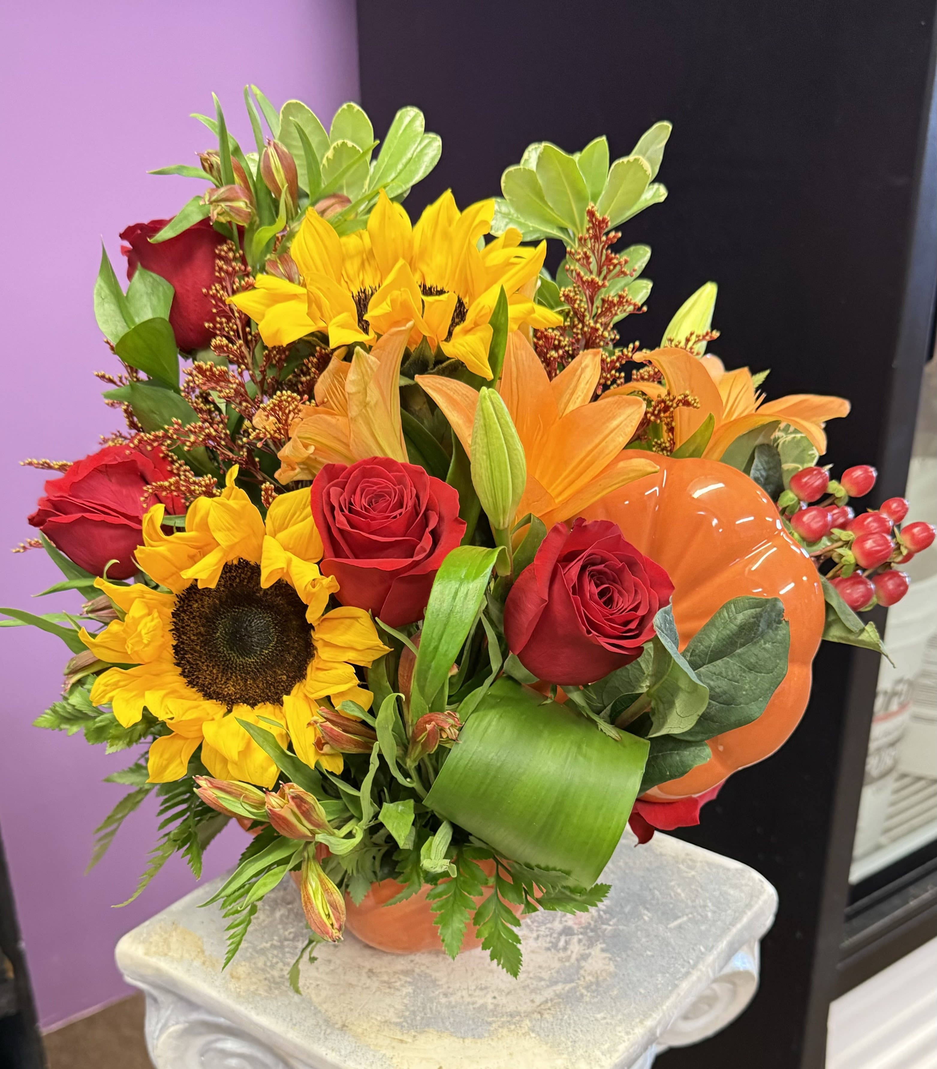 Bouquet of sunflowers, red roses, and orange lilies in a pumpkin vase