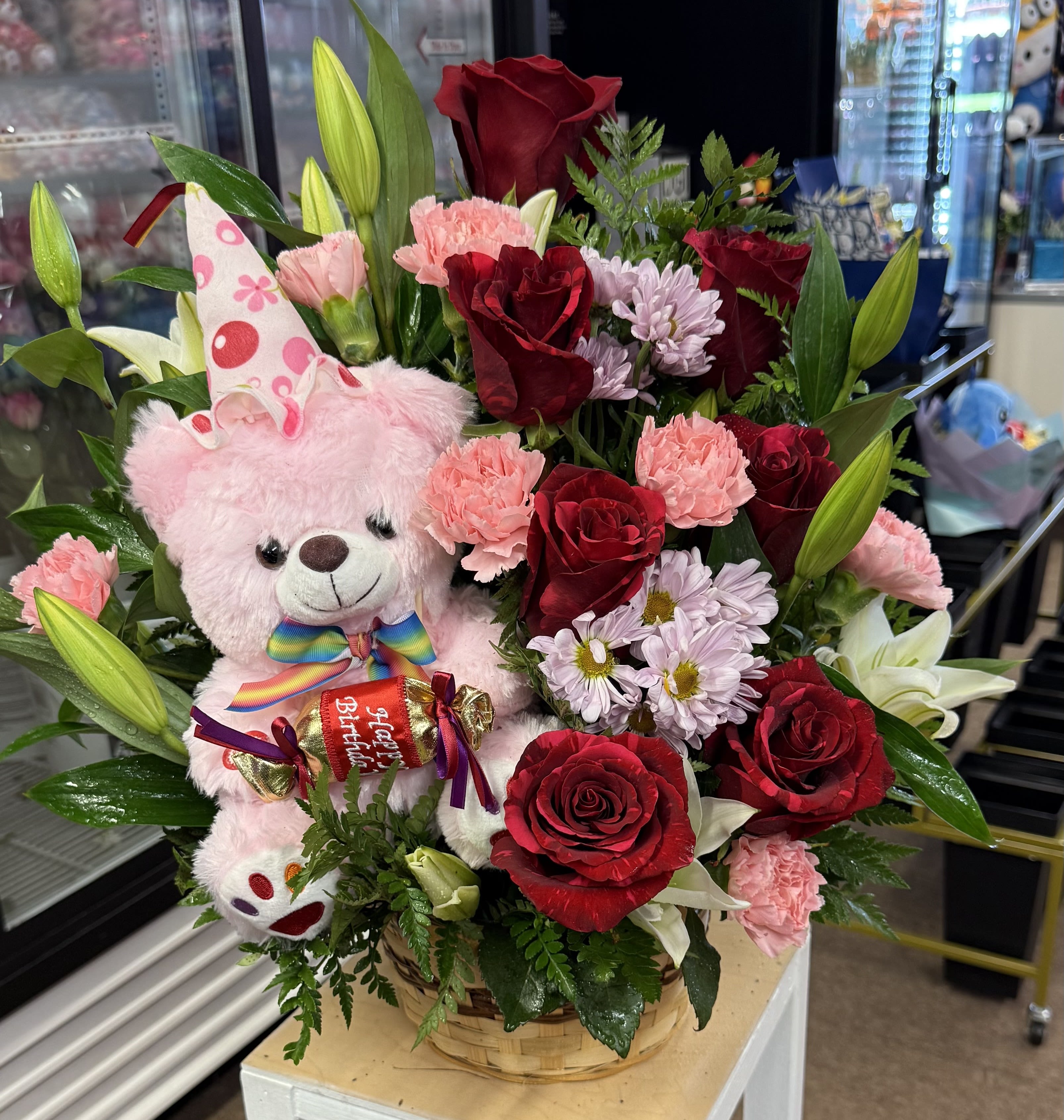 Basket arrangement with red roses, pink carnations, lilies, and a pink teddy bear