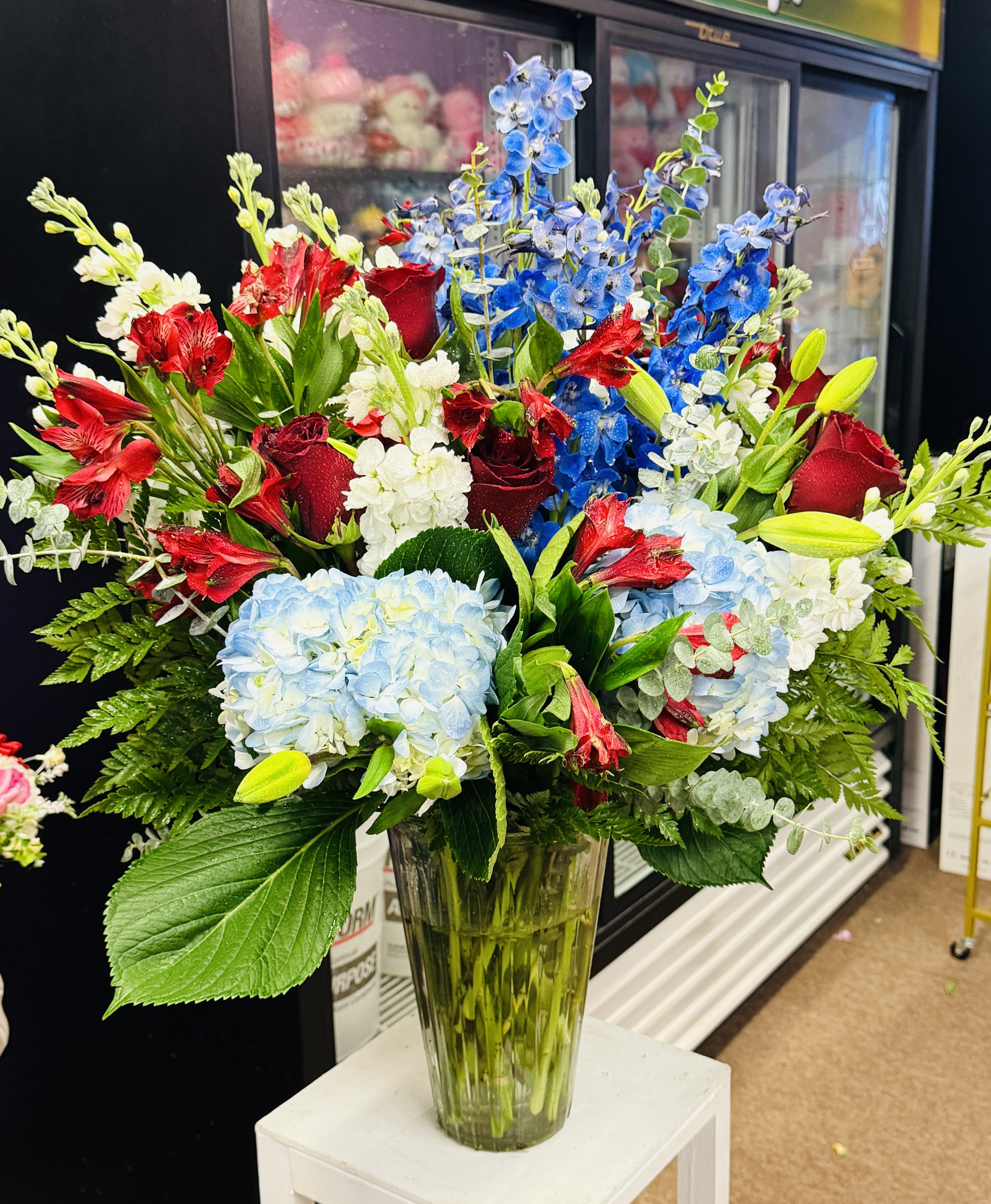 Mixed bouquet of red roses, blue delphinium, and pale hydrangeas in a glass vase