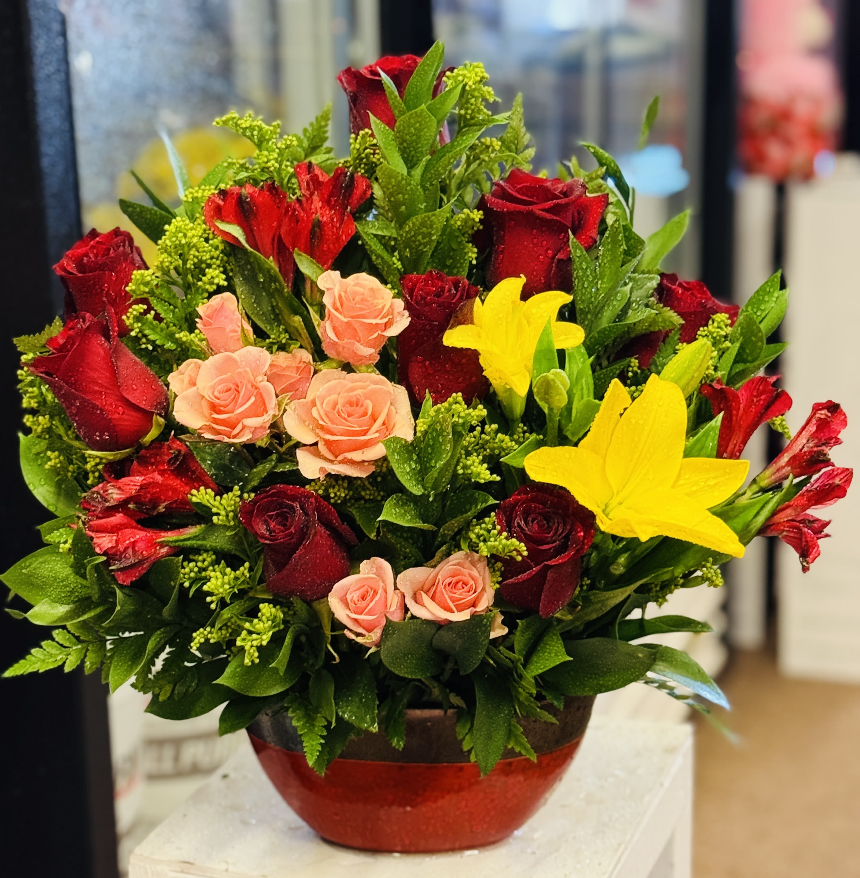 Red and peach roses with yellow lilies in a red vase