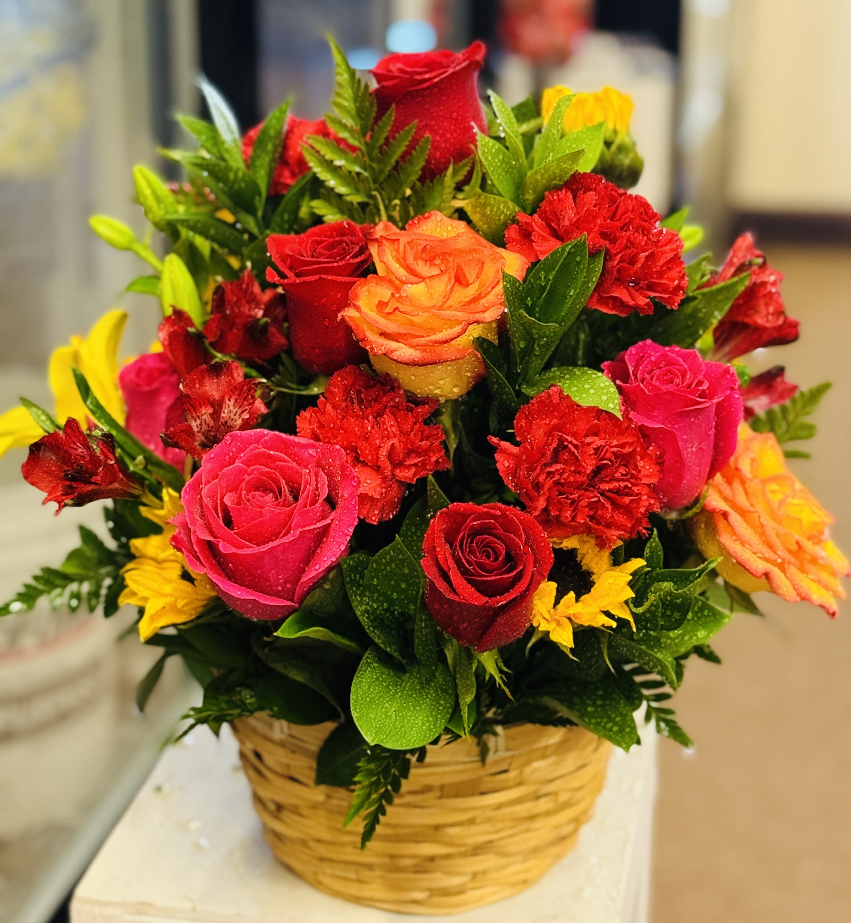 Basket arrangement of red, pink, orange, and yellow roses with carnations