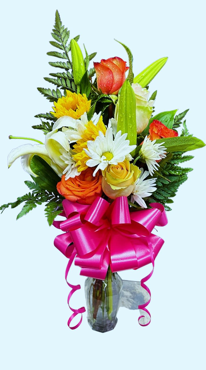 Mixed bouquet of roses, lilies, and daisies in a glass vase with a pink ribbon