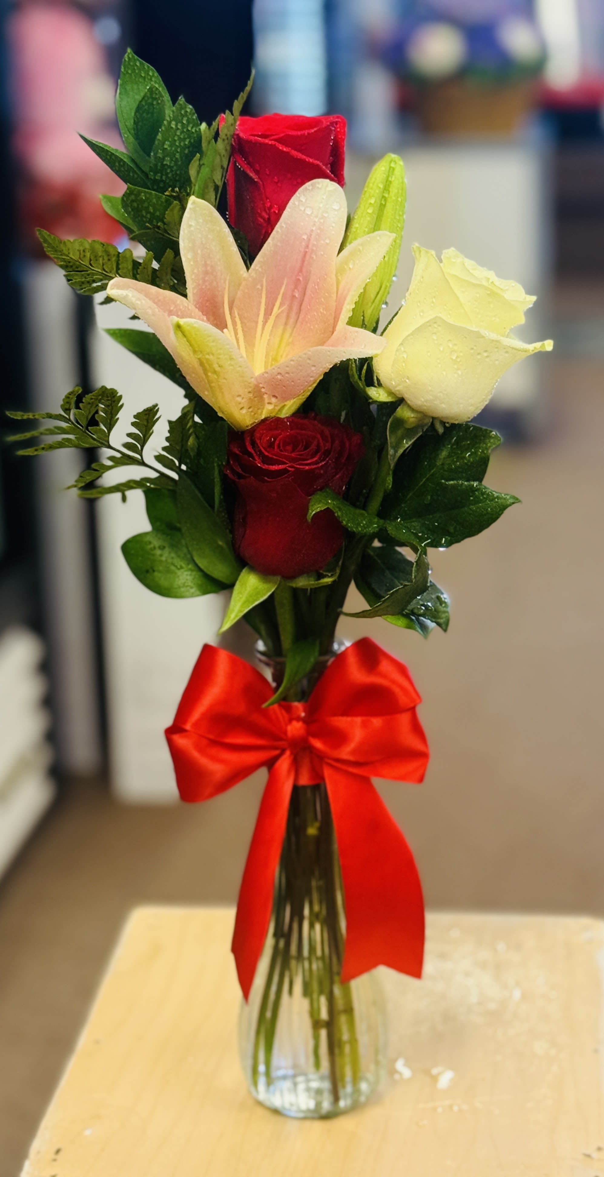 Bouquet of red roses and a pink lily in a glass vase with a red bow