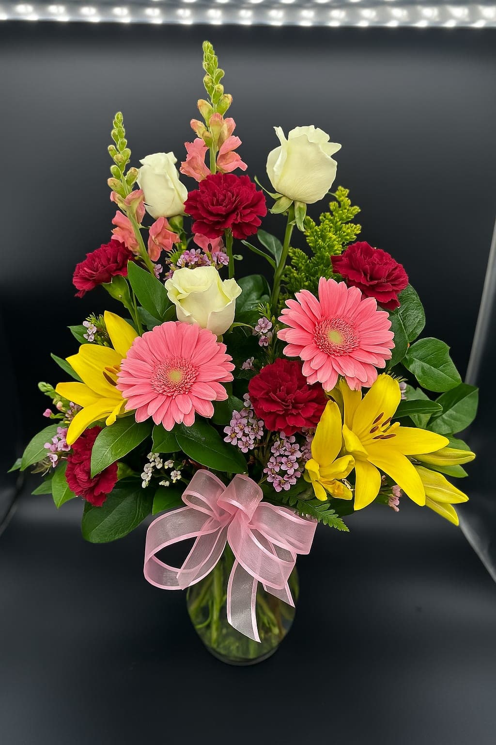 Perfect Touch - Soft pinks, bold reds, sunny yellows, and elegant whites—this radiant arrangement is a celebration of joy, love, and fresh beginnings. Accented with a delicate pink bow, it’s the perfect touch of beauty for any moment worth remembering!