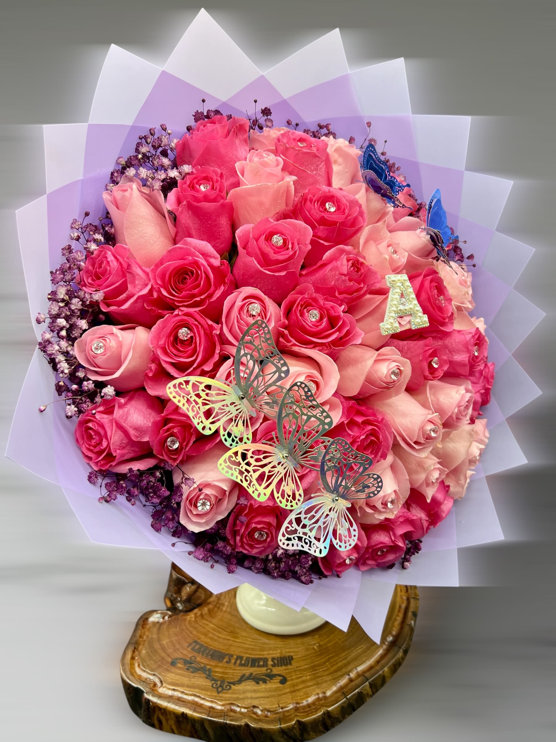 Love For Ever -  A bouquet that speaks elegance and charm!   This stunning arrangement of pink and blush roses, accented with sparkling rhinestones, delicate baby’s breath, and whimsical butterflies, is the perfect gift for someone truly special. The soft lavender wrap and personalized touches like the glitter “A” make it uniquely thoughtful. Ideal for birthdays, anniversaries, or just to say “you’re  Love.  50 Roses Count. STANDARD 100 Deluxe