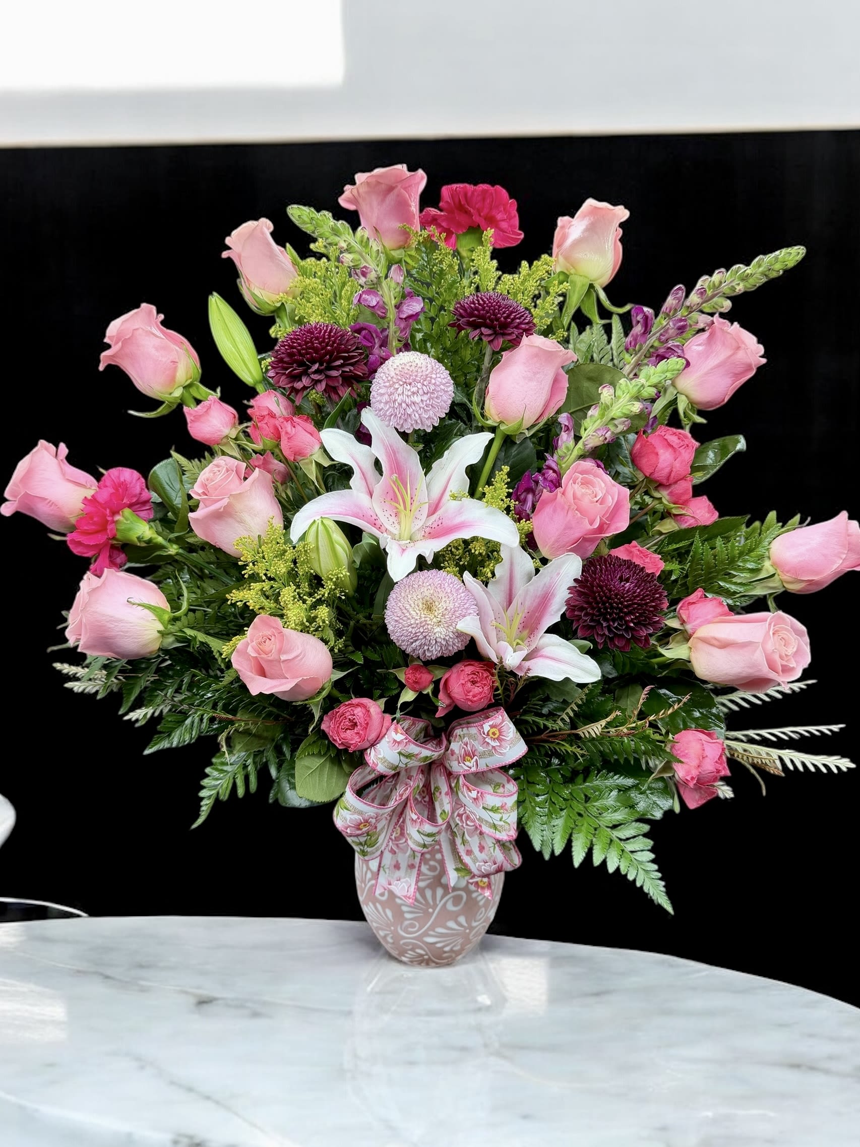 Pink roses and lilies arranged in a decorative vase with a ribbon