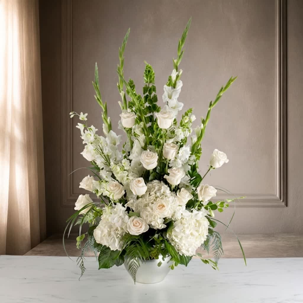 Sweet Comfort by BloomNation™ (DL) - The Sweet Comfort sympathy flowers arrangement is a delicate and soothing tribute that combines the elegance of all-white flowers, including roses, hydrangeas, gladiolas, and larkspur. This arrangement exudes a sense of peace, serenity, and comfort, offering solace and support during a time of loss and grief.