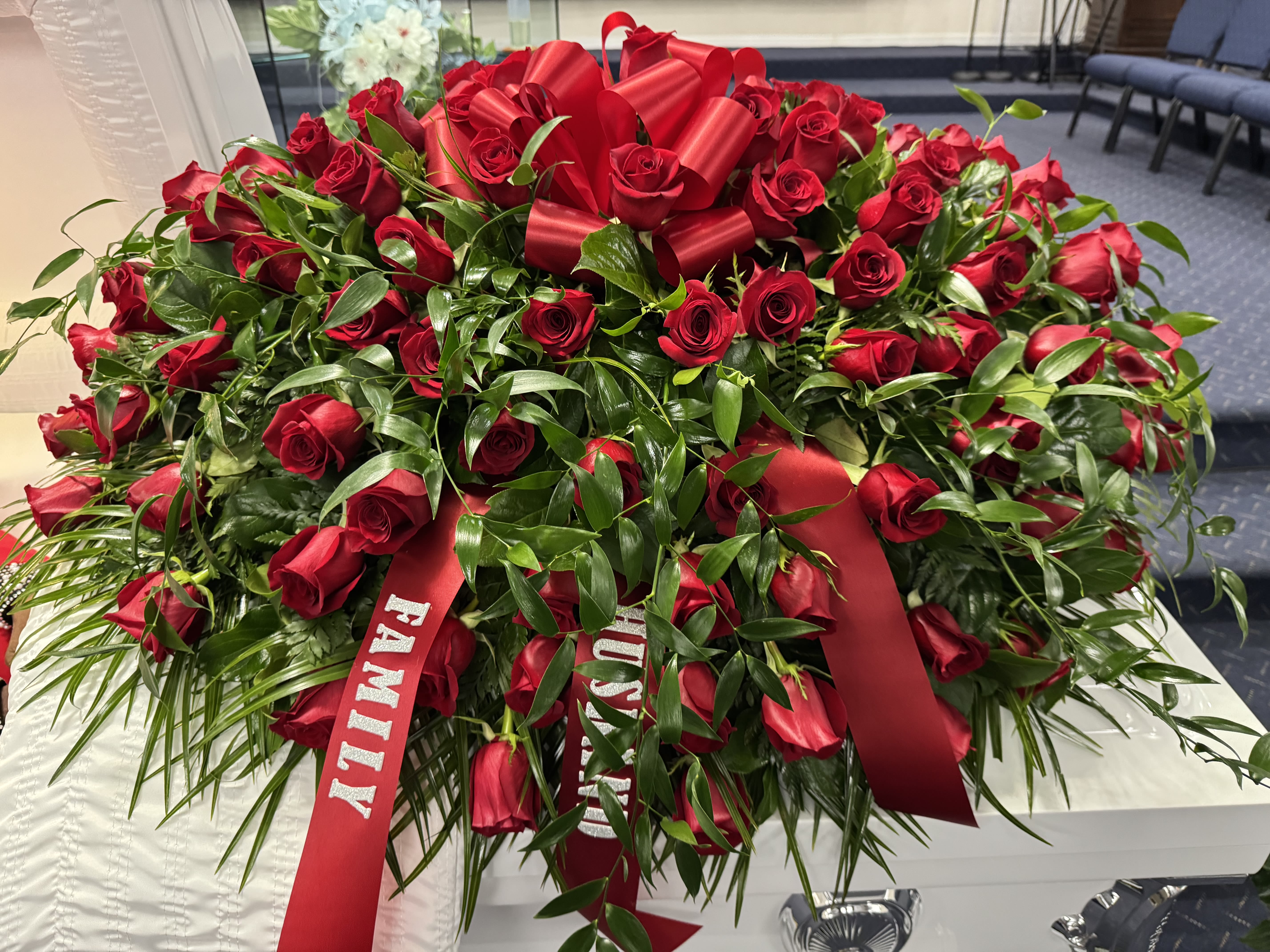 Large red rose arrangement with satin ribbons on a casket