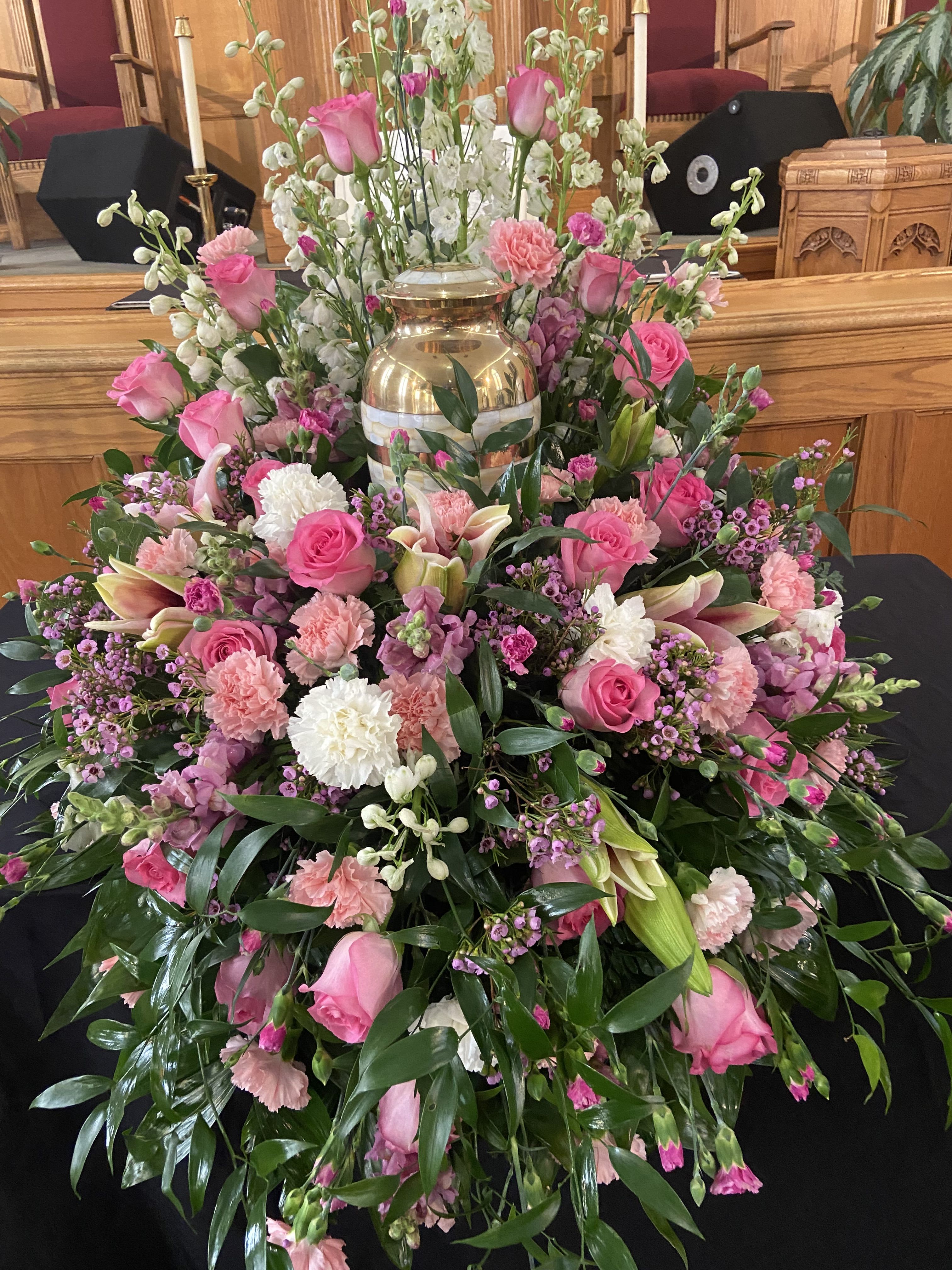 Large pink and white floral funeral arrangement with a gold urn centerpiece