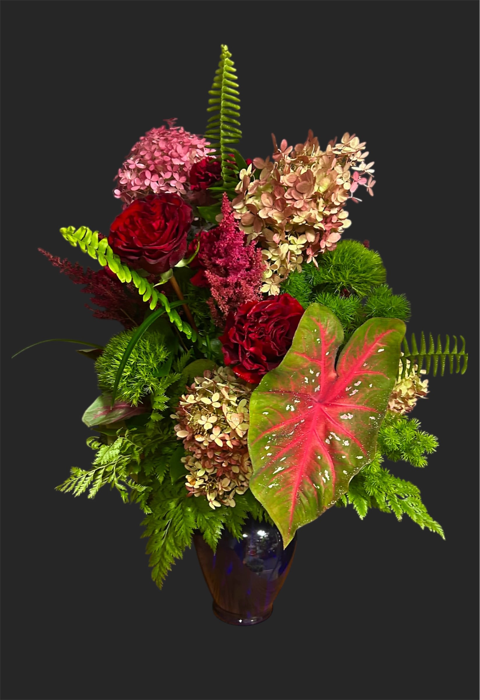 Red roses and pink hydrangeas in a dark glass vase