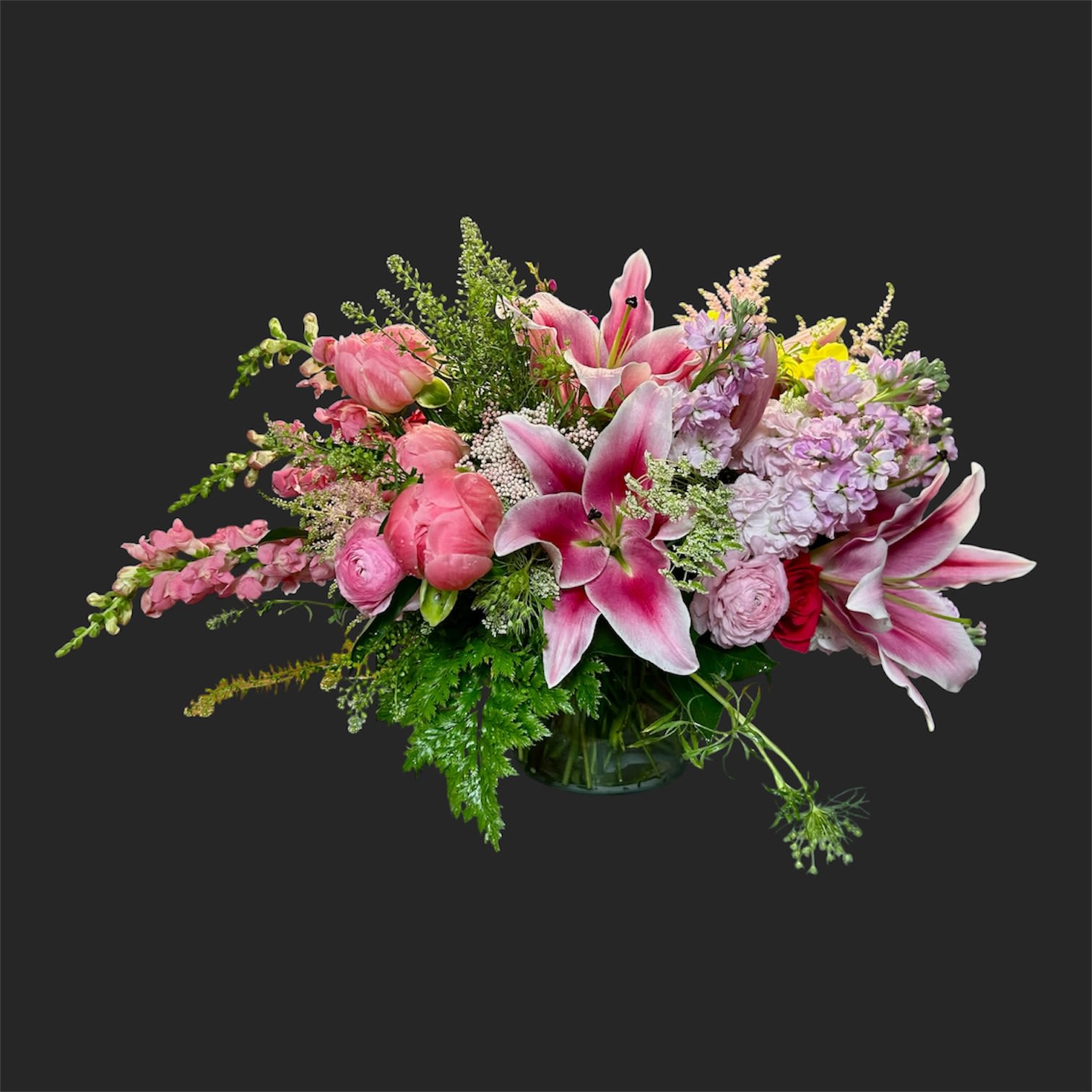 Beautiful and Grand - Large pink stargazer lilies take center stage in this flower arrangement, making it an unforgettable birthday bouquet or anniversary gift that reads romantic and celebratory from across the room. The asymmetrical, garden-style design pairs those lilies with soft pink tulips, creamy ranunculus, and clusters of lavender stock and snapdragons so the person you're surprising will feel genuinely celebrated and seen.