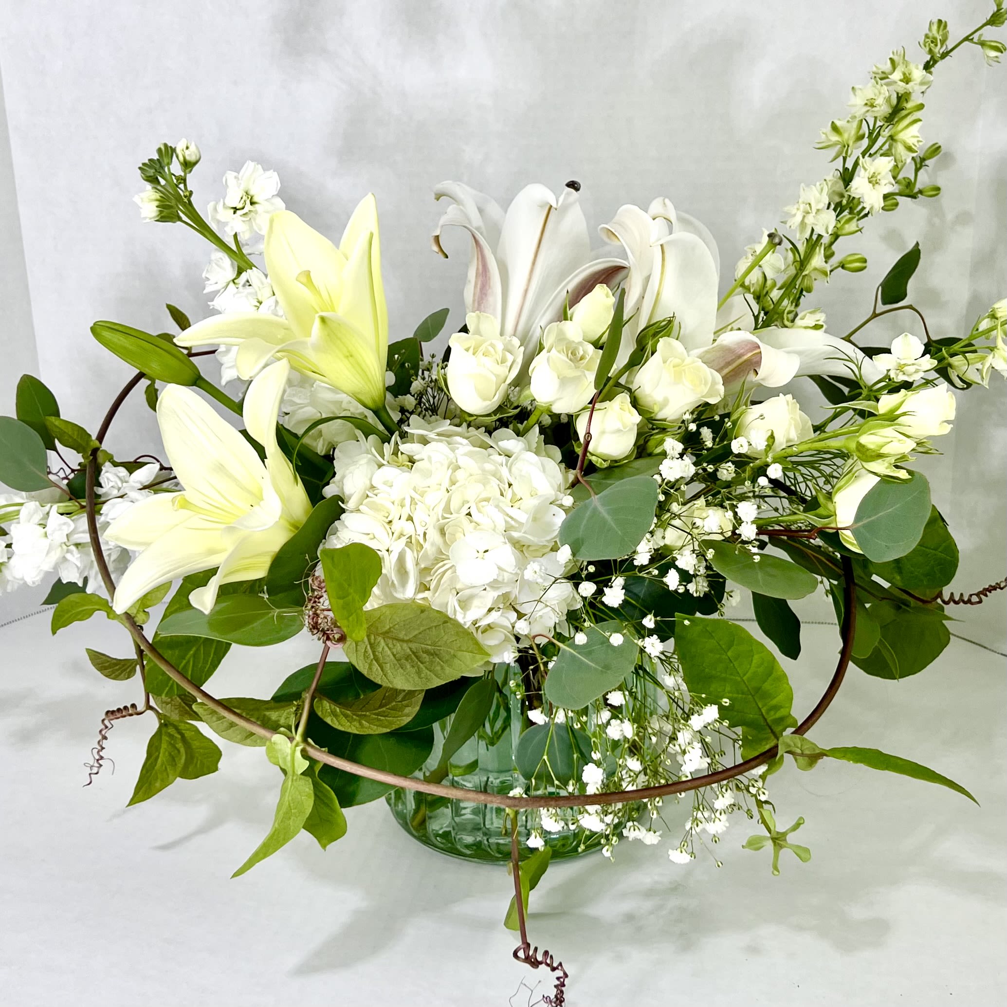 White lilies and roses arranged in a glass vase with greenery