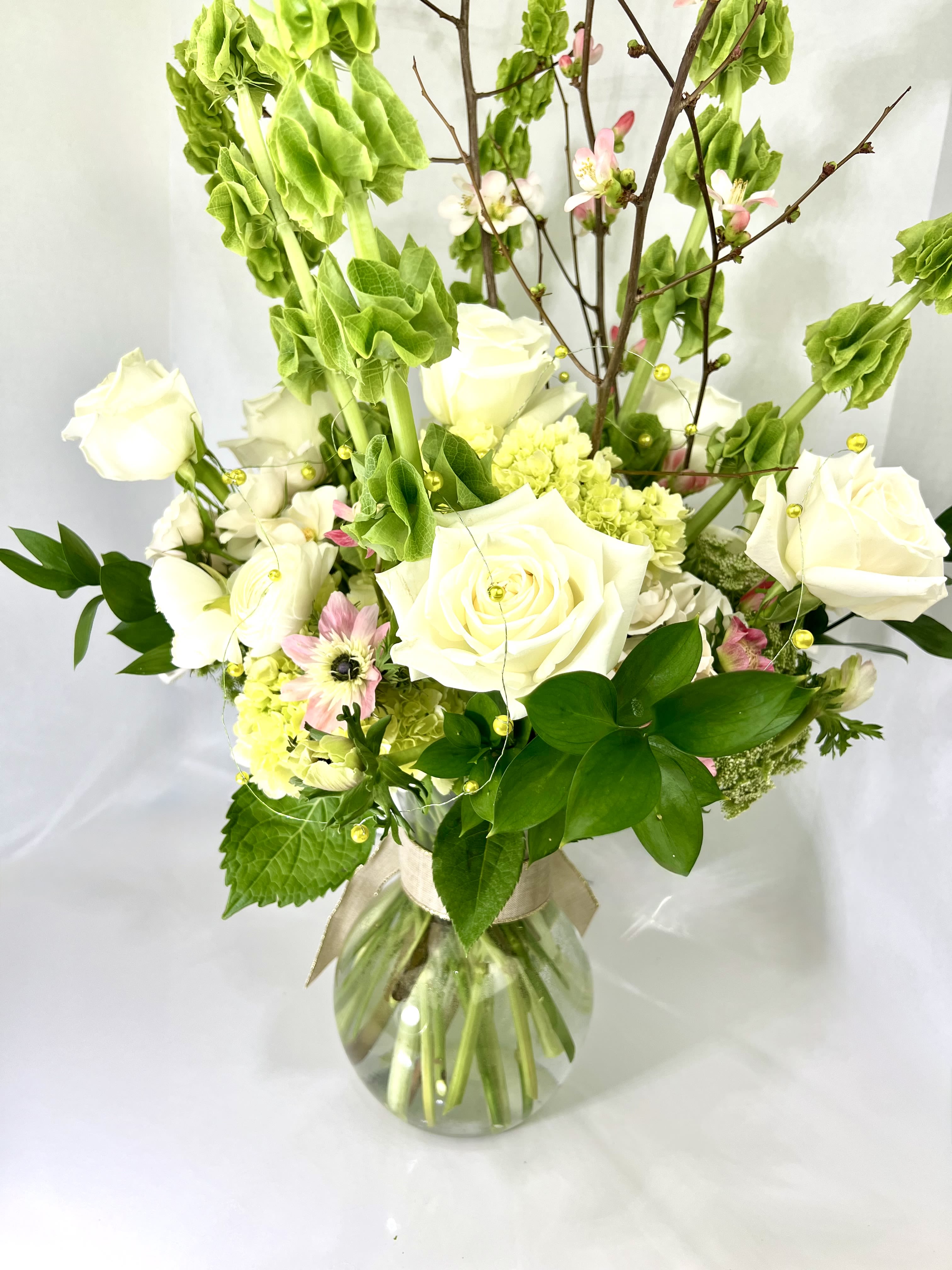 White roses and pink blossoms in a glass vase with tall green stems