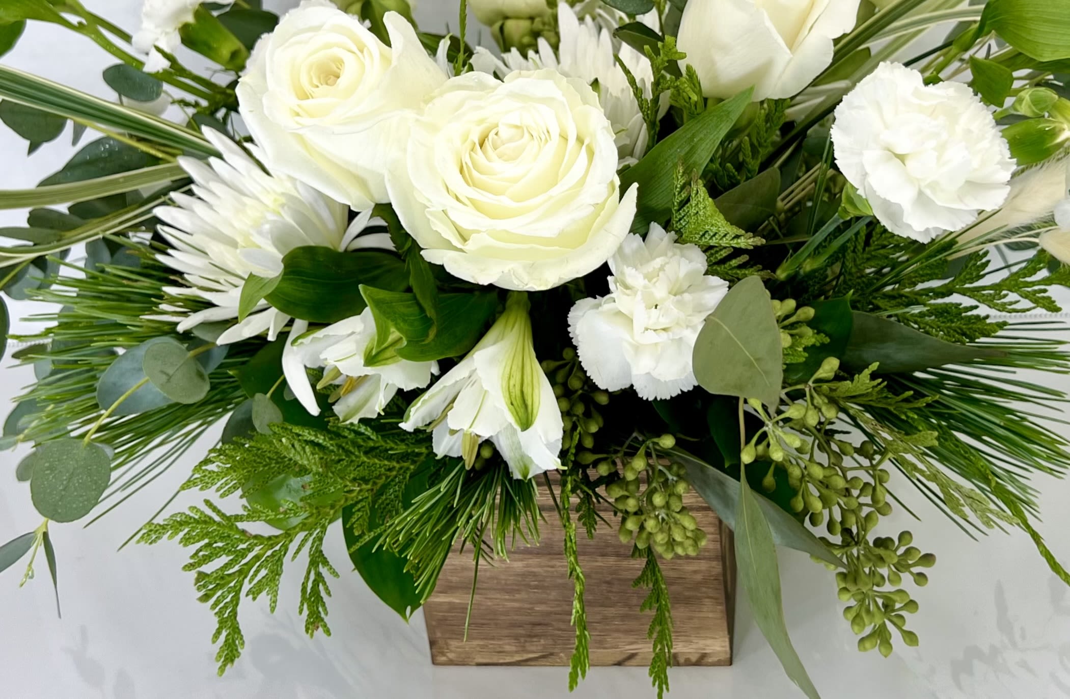 White roses and lilies in a wooden box with greenery