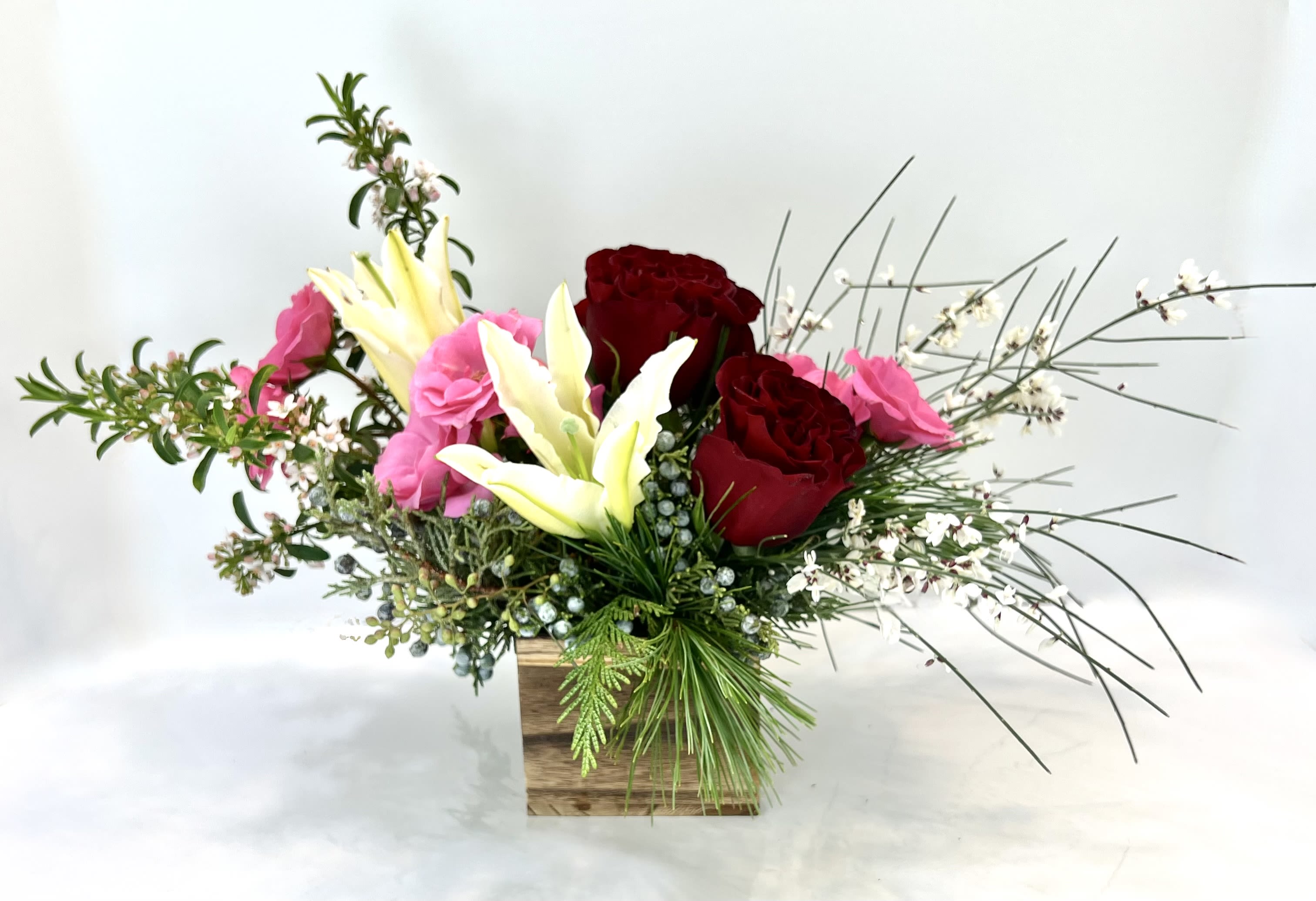 Arrangement of red and pink roses with white lilies in a wooden box