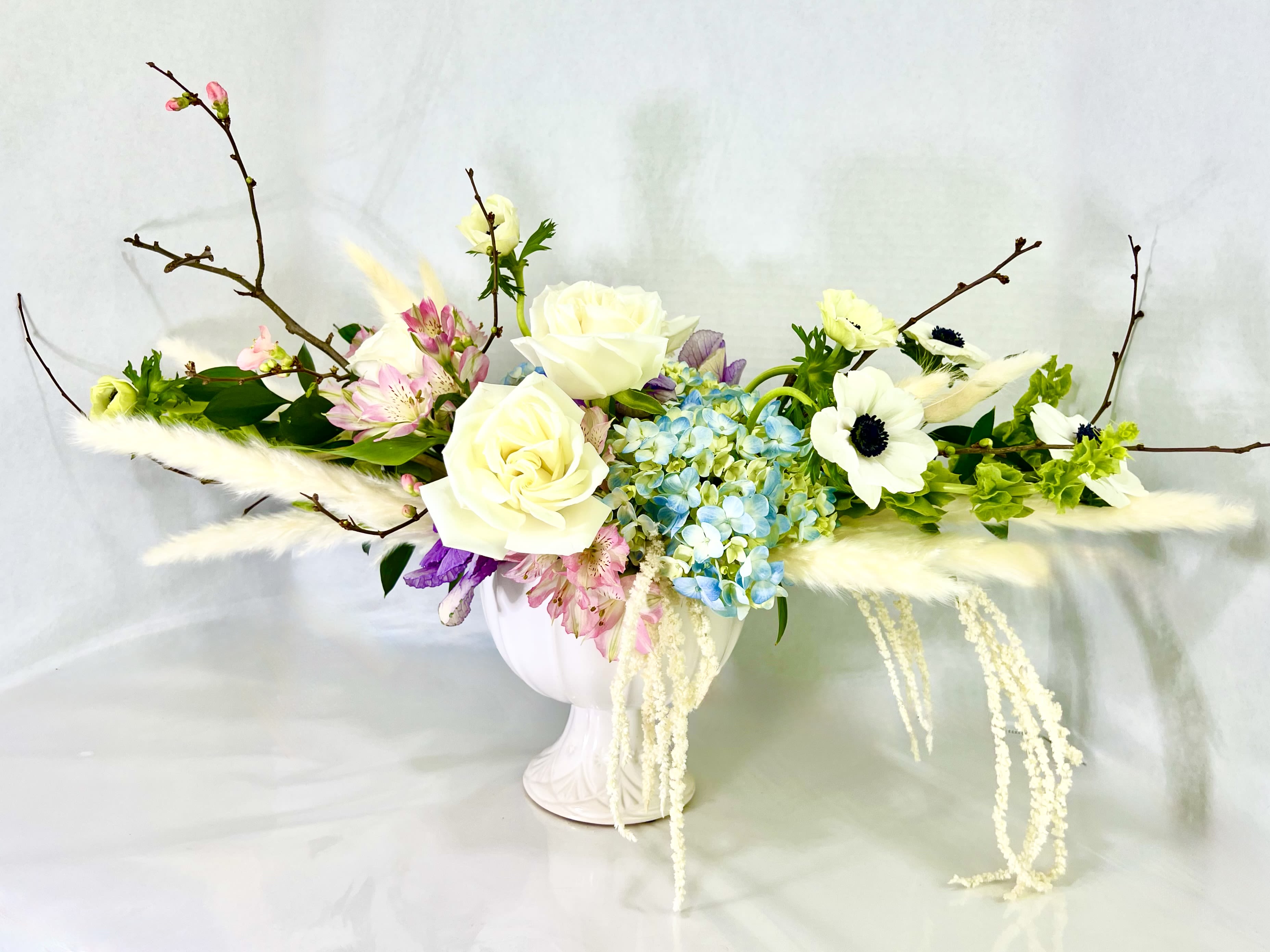 White roses and blue hydrangeas in a white vase with branches and feathers
