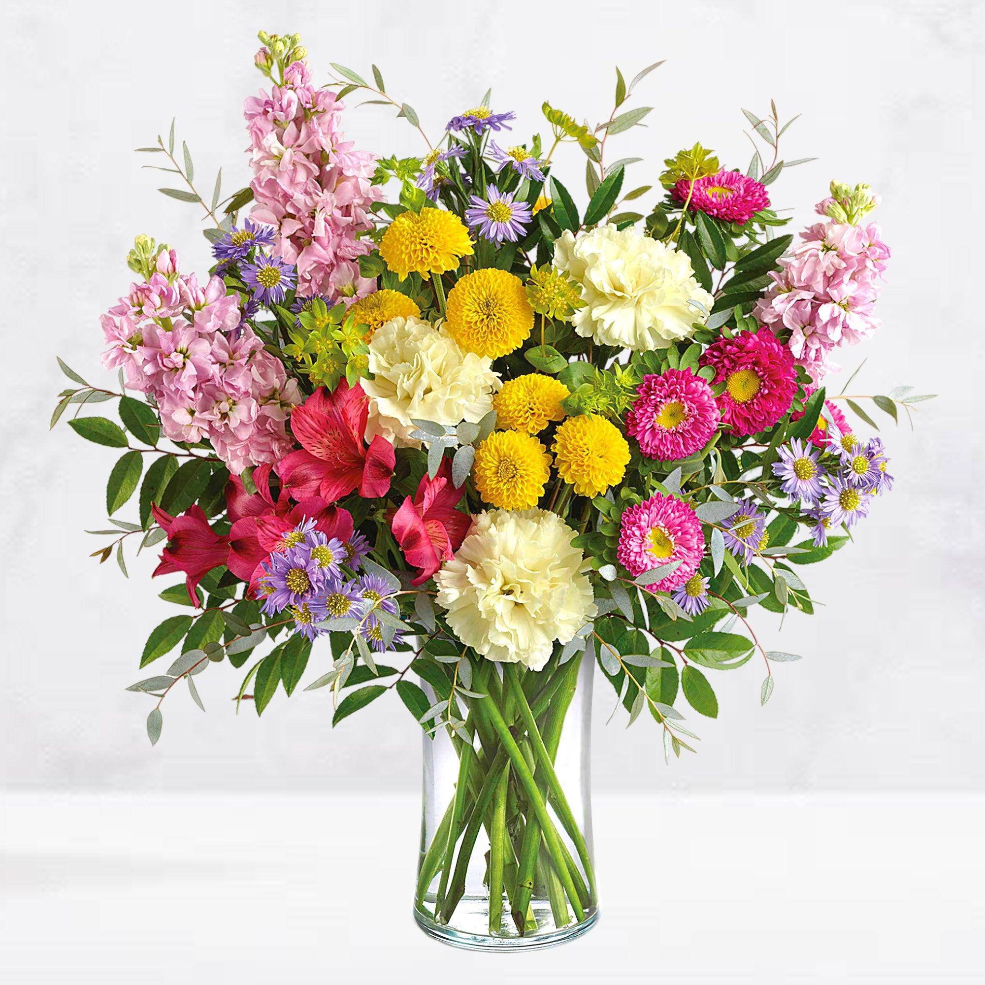 Mixed bouquet of pink, yellow, white, and purple flowers in a glass vase