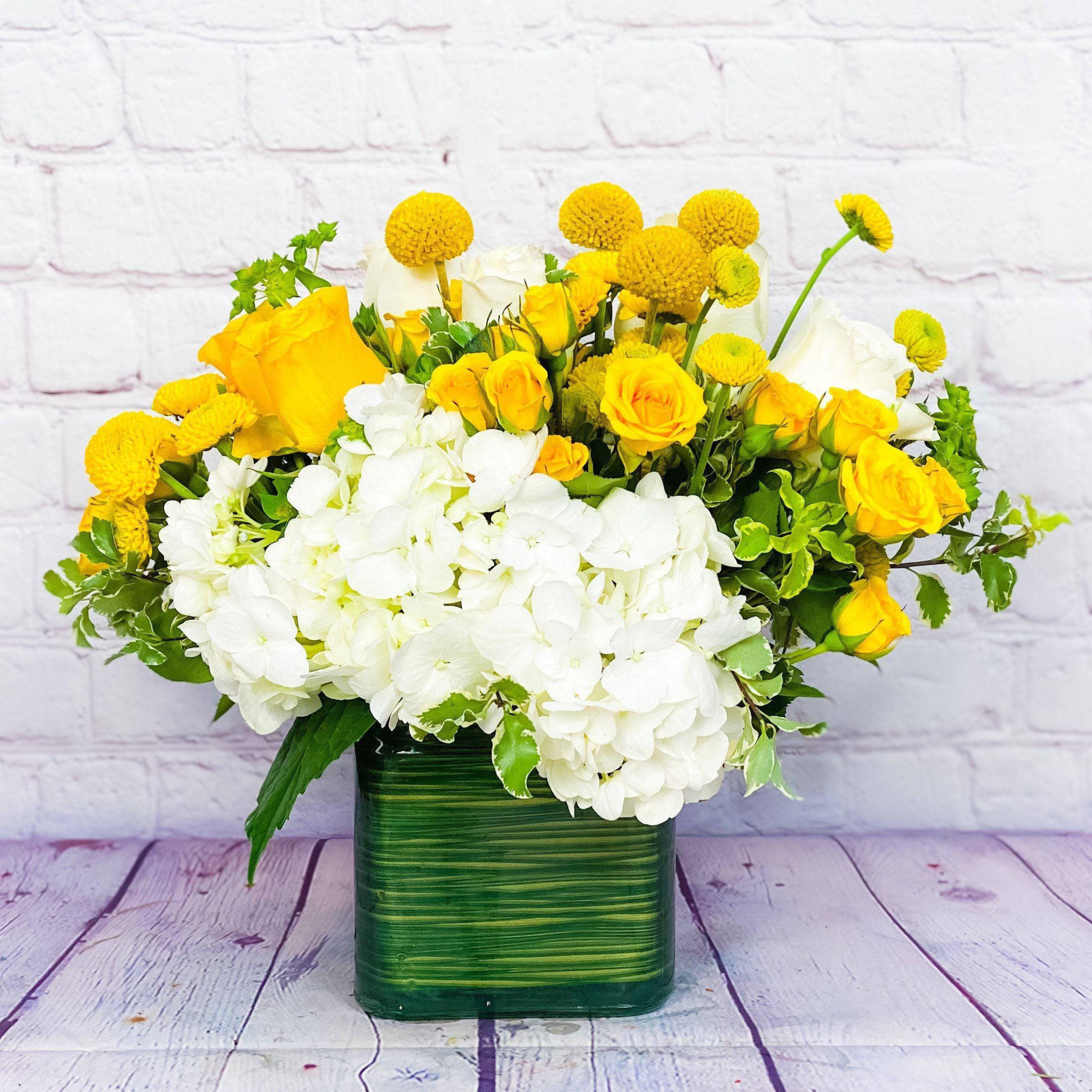 Yellow roses and white hydrangeas in a green square vase