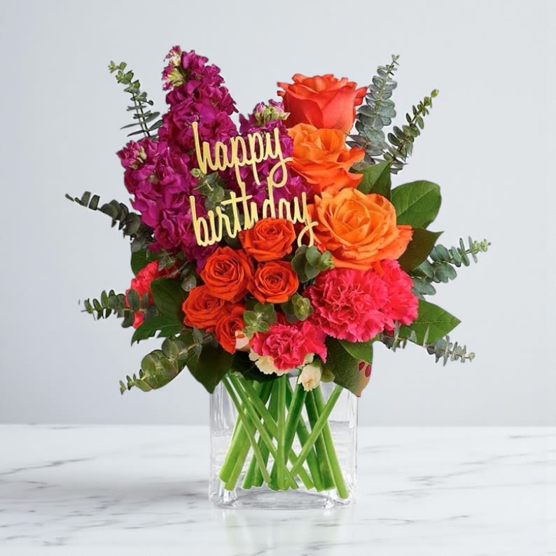 Bouquet of orange and pink flowers in a clear glass vase with a "happy birthday" sign