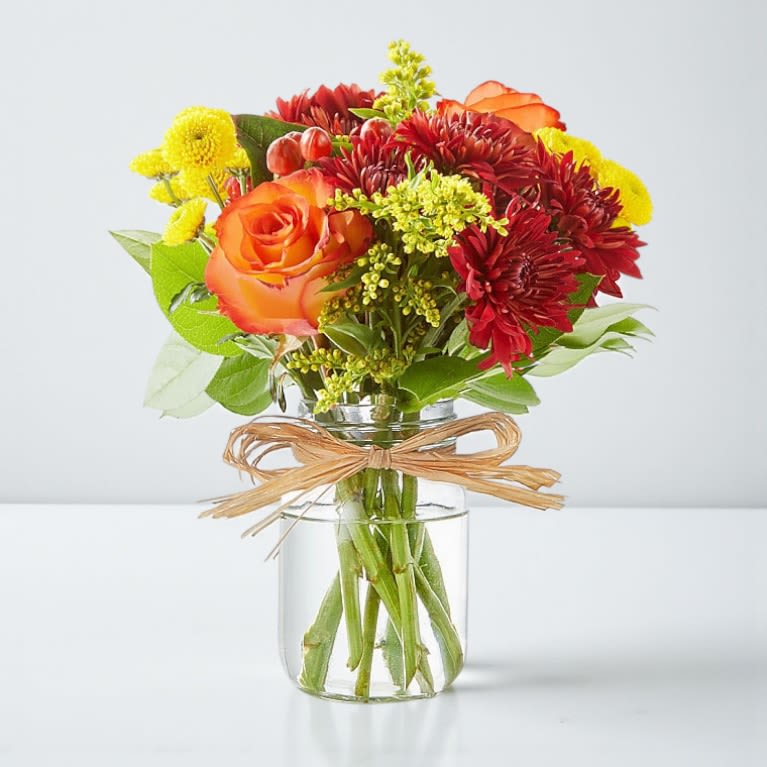 Harvest Charm Bouquet - Celebrate the warmth of fall with our Harvest Charm Bouquet. This seasonal favorite blends rich roses, cheerful mums, and golden solidago, beautifully arranged in a rustic mason jar. Inspired by the simple joys of apple picking, this bouquet brings autumn’s cozy charm right to your home.
