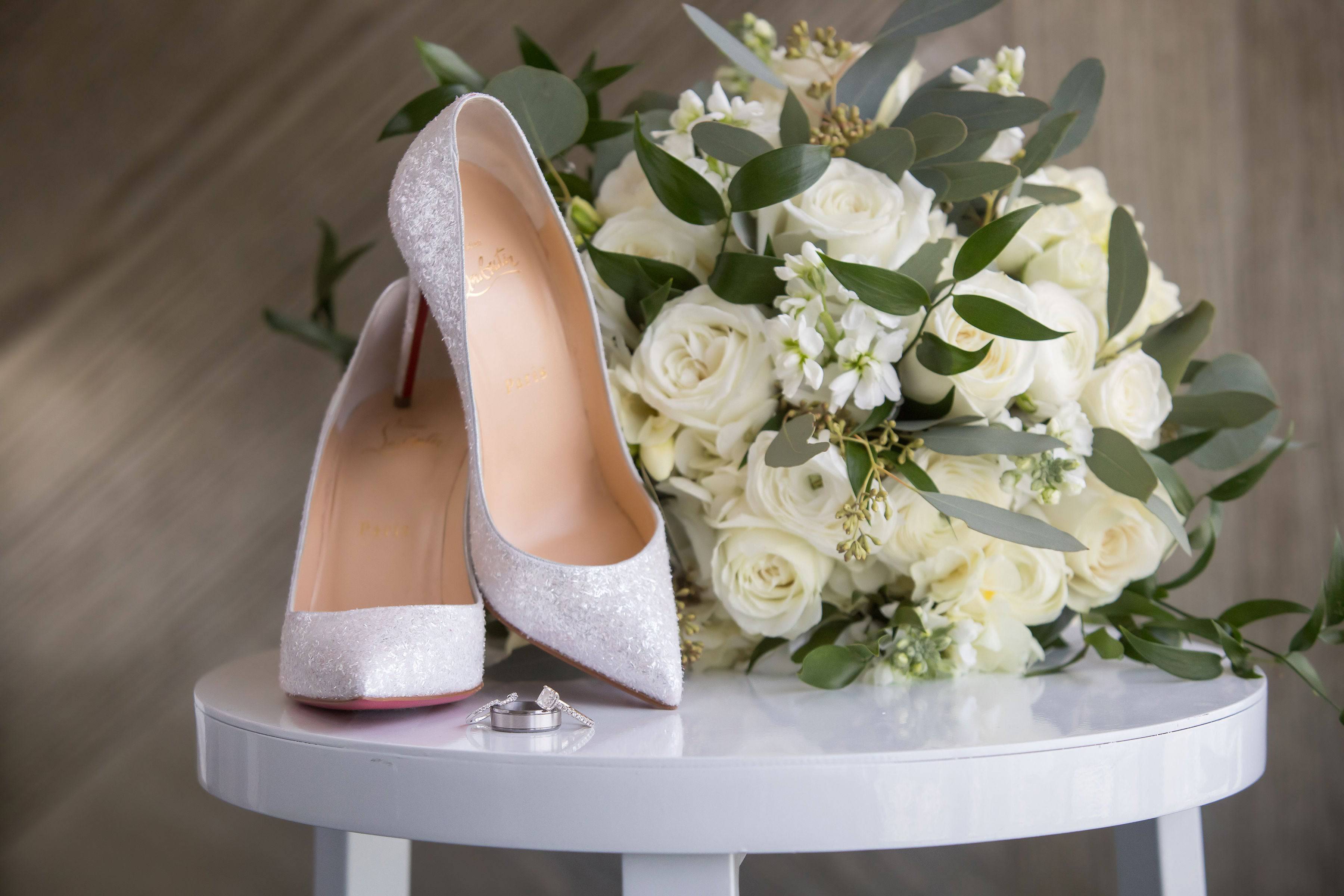White rose bouquet with silver high heels and wedding rings on a table