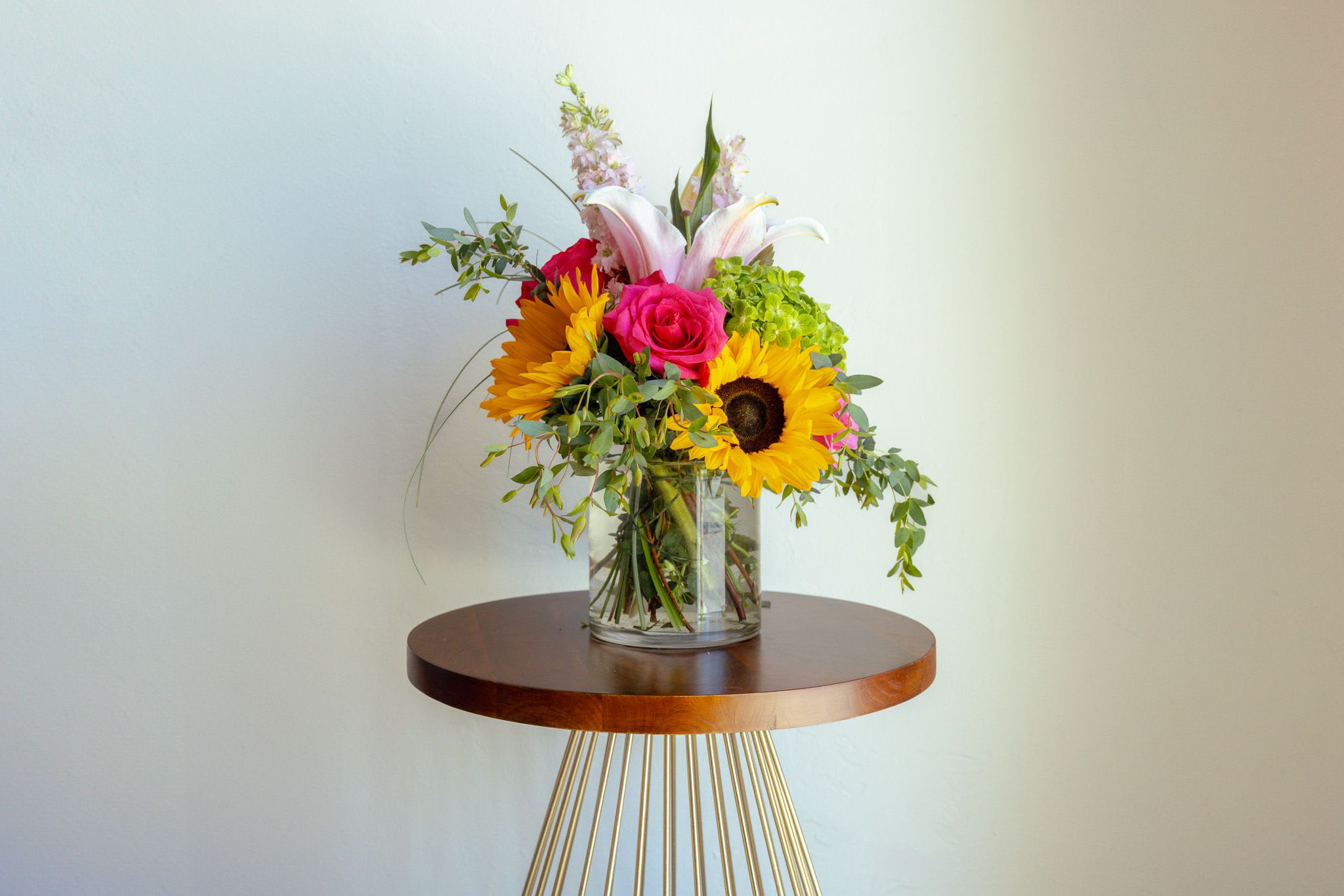 Mixed bouquet in a clear glass vase with sunflowers, roses, and lilies