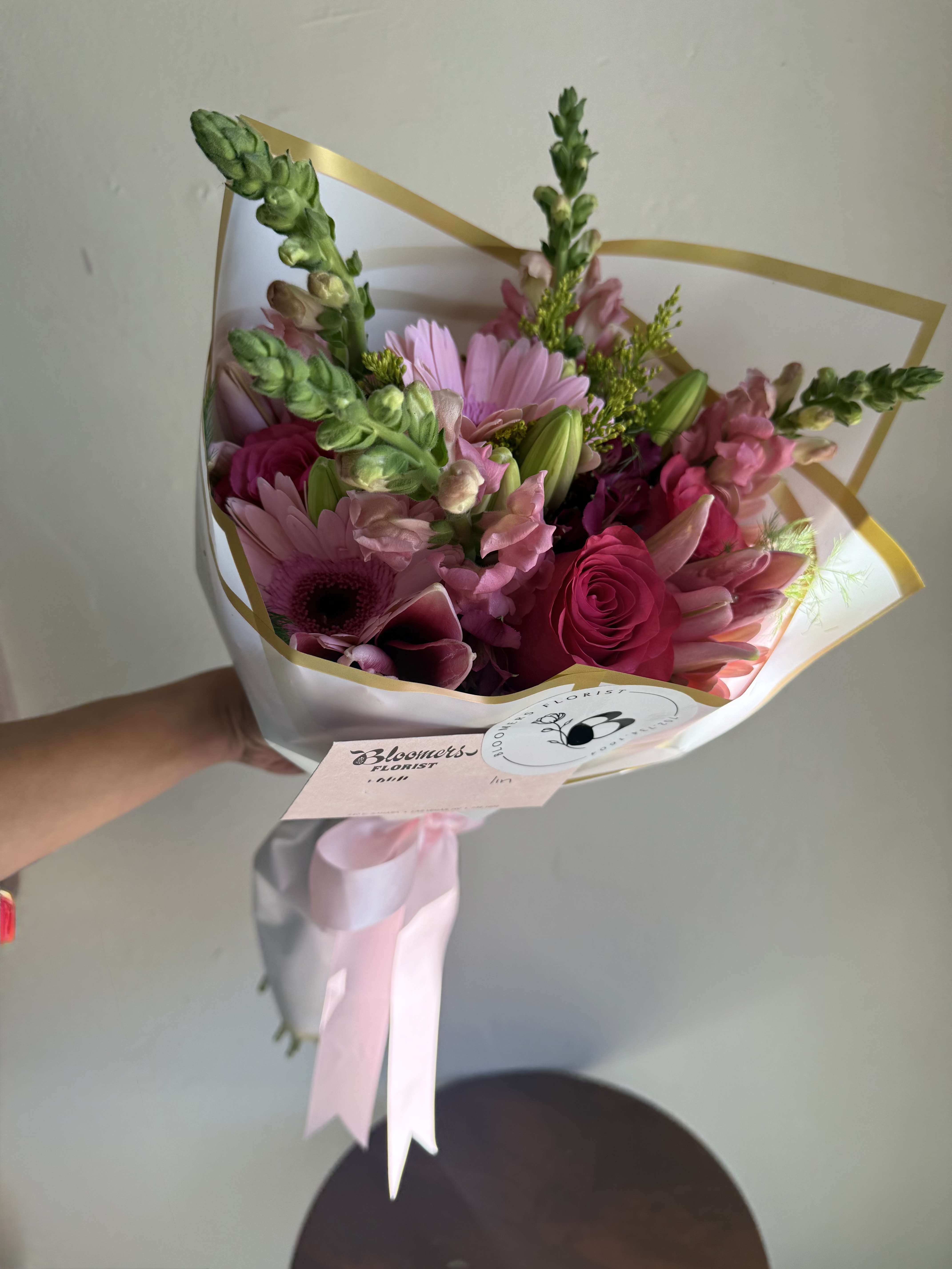Pink mixed flower bouquet wrapped in white paper with a pink ribbon