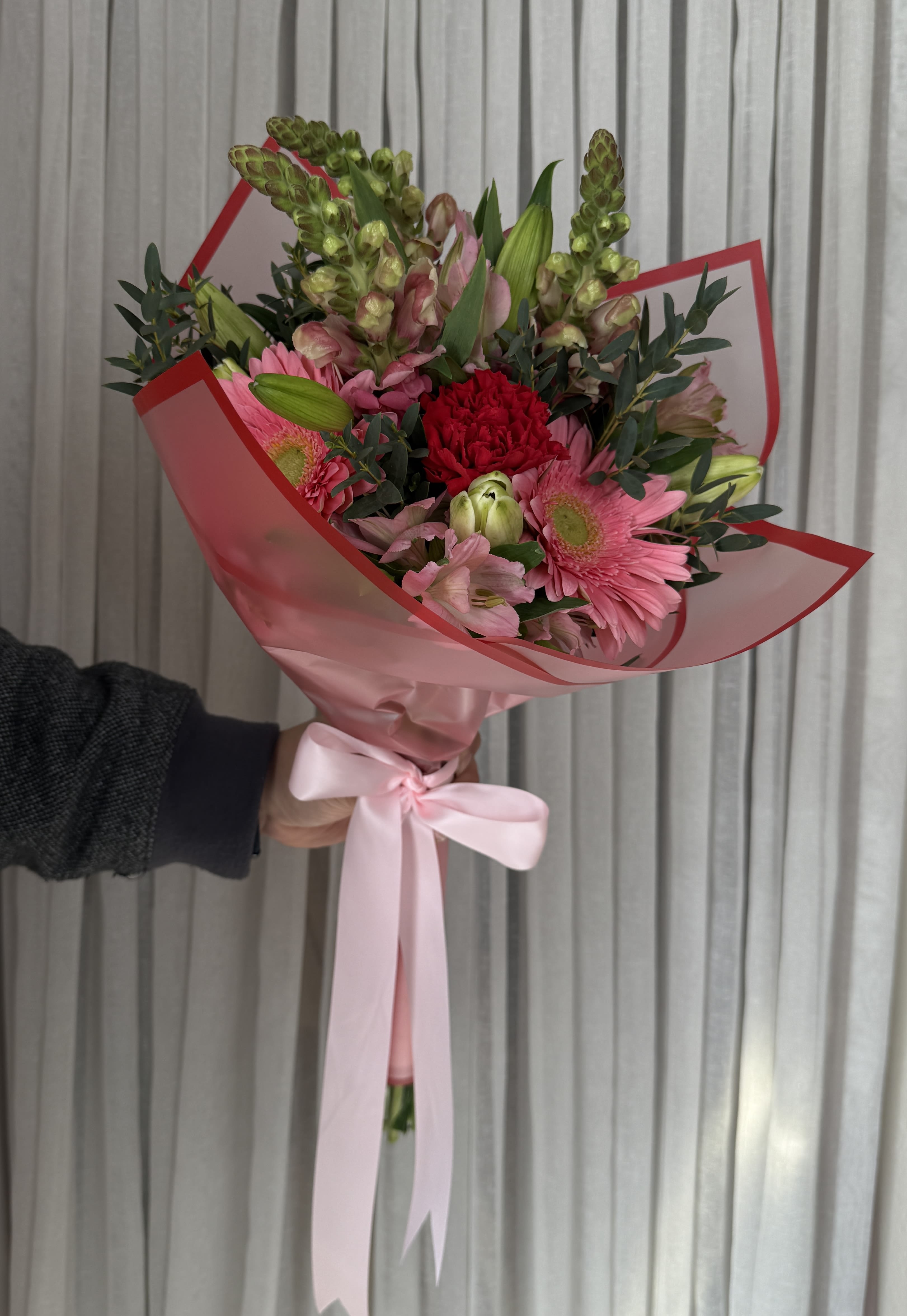 Handheld bouquet of pink and red flowers wrapped in pink paper with a ribbon