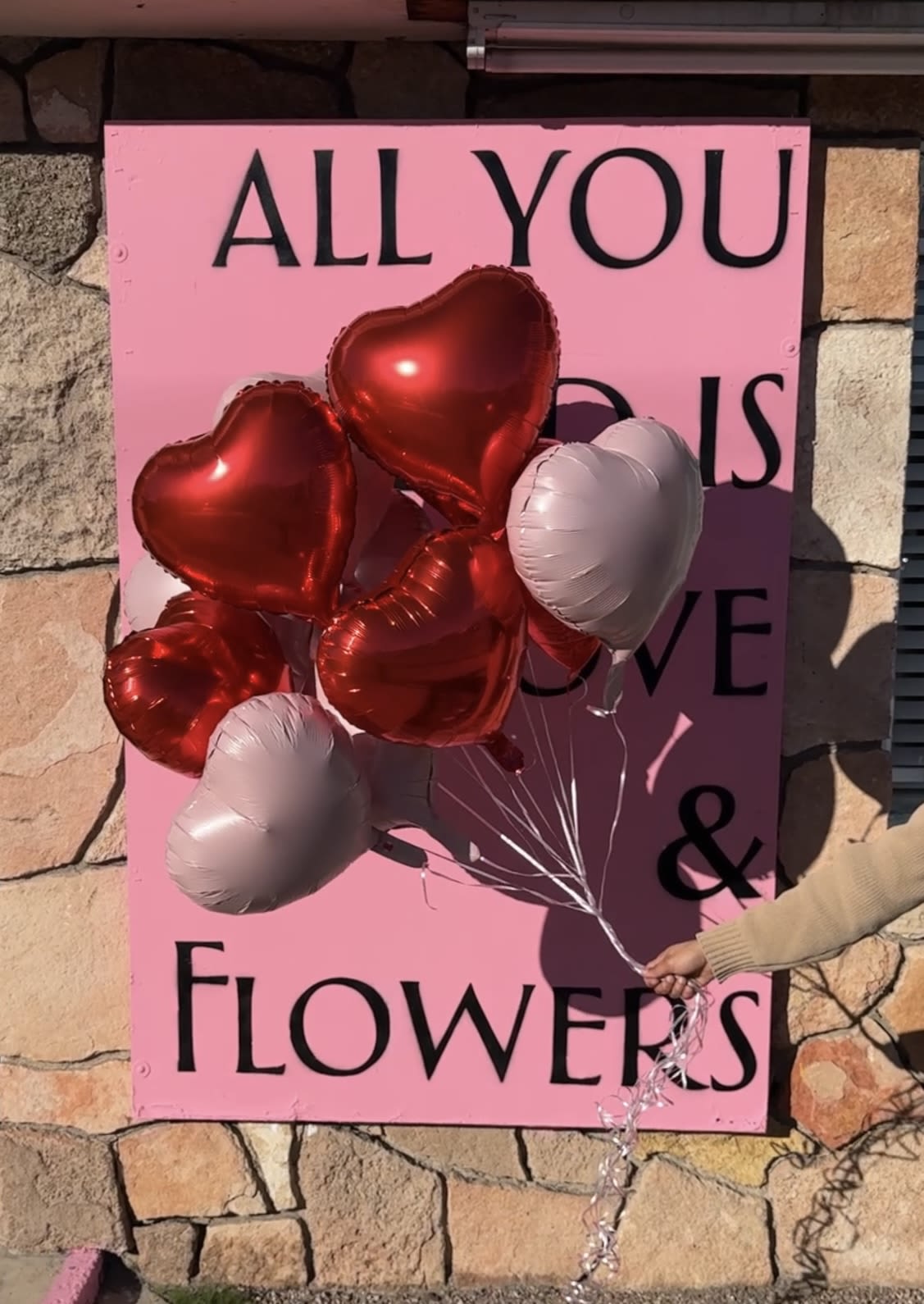 Heart-shaped balloons in red and white held in front of a pink sign