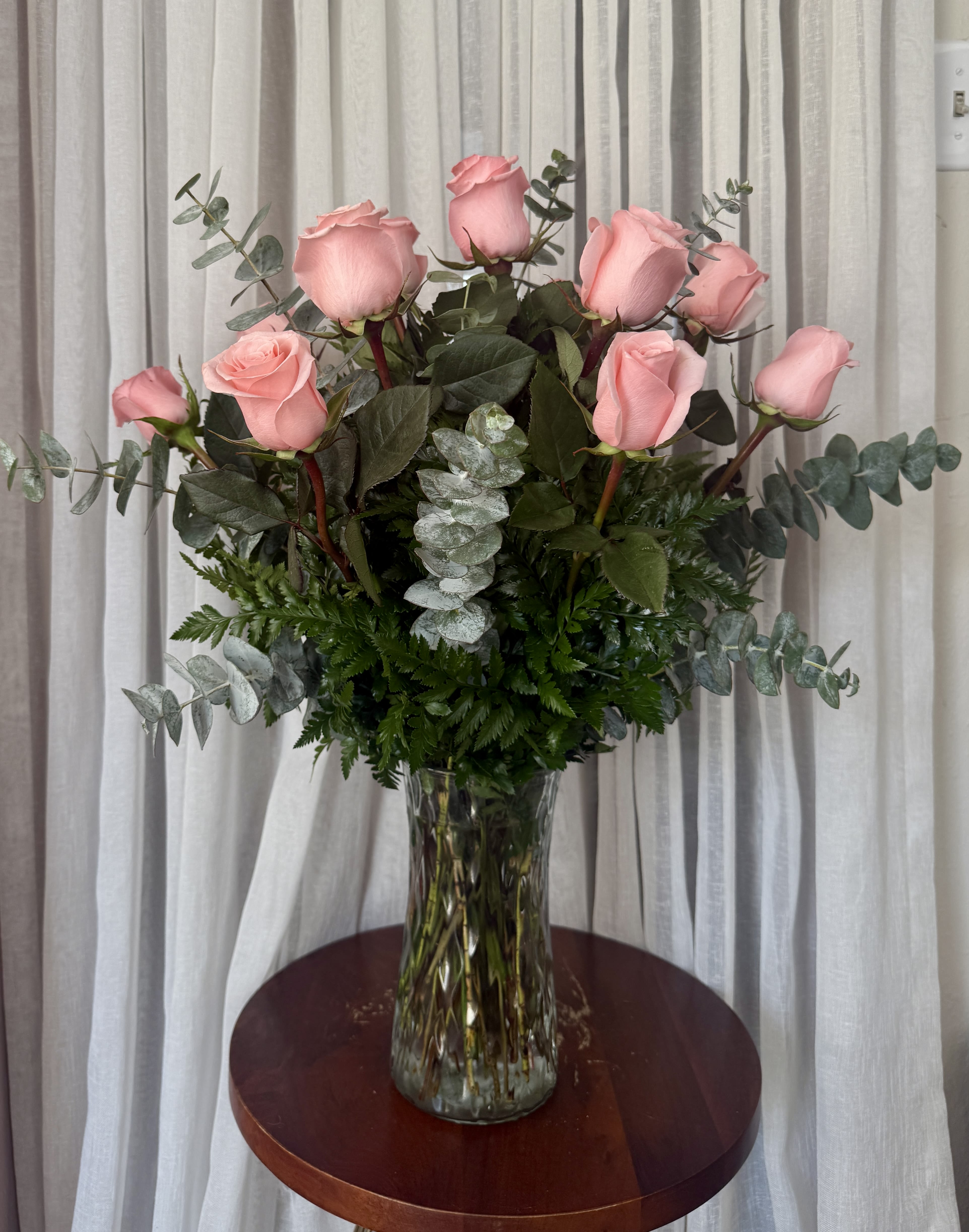 Pink roses arranged in a clear glass vase with eucalyptus foliage