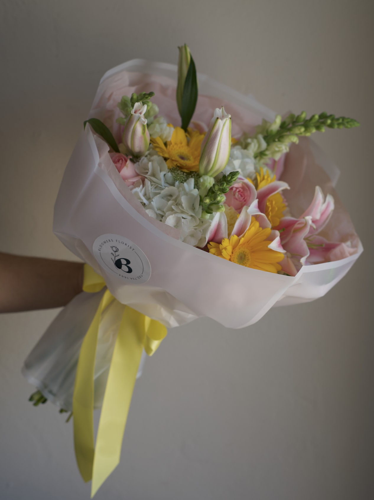Bouquet of pink and yellow flowers wrapped in pale pink paper with a yellow ribbon