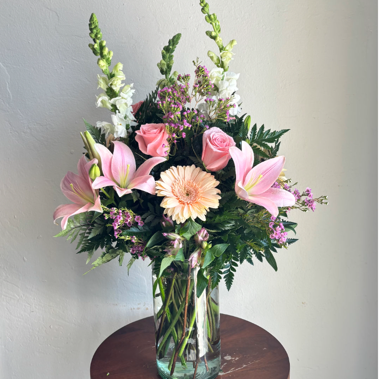 Pink lilies, roses, and a peach gerbera in a glass vase