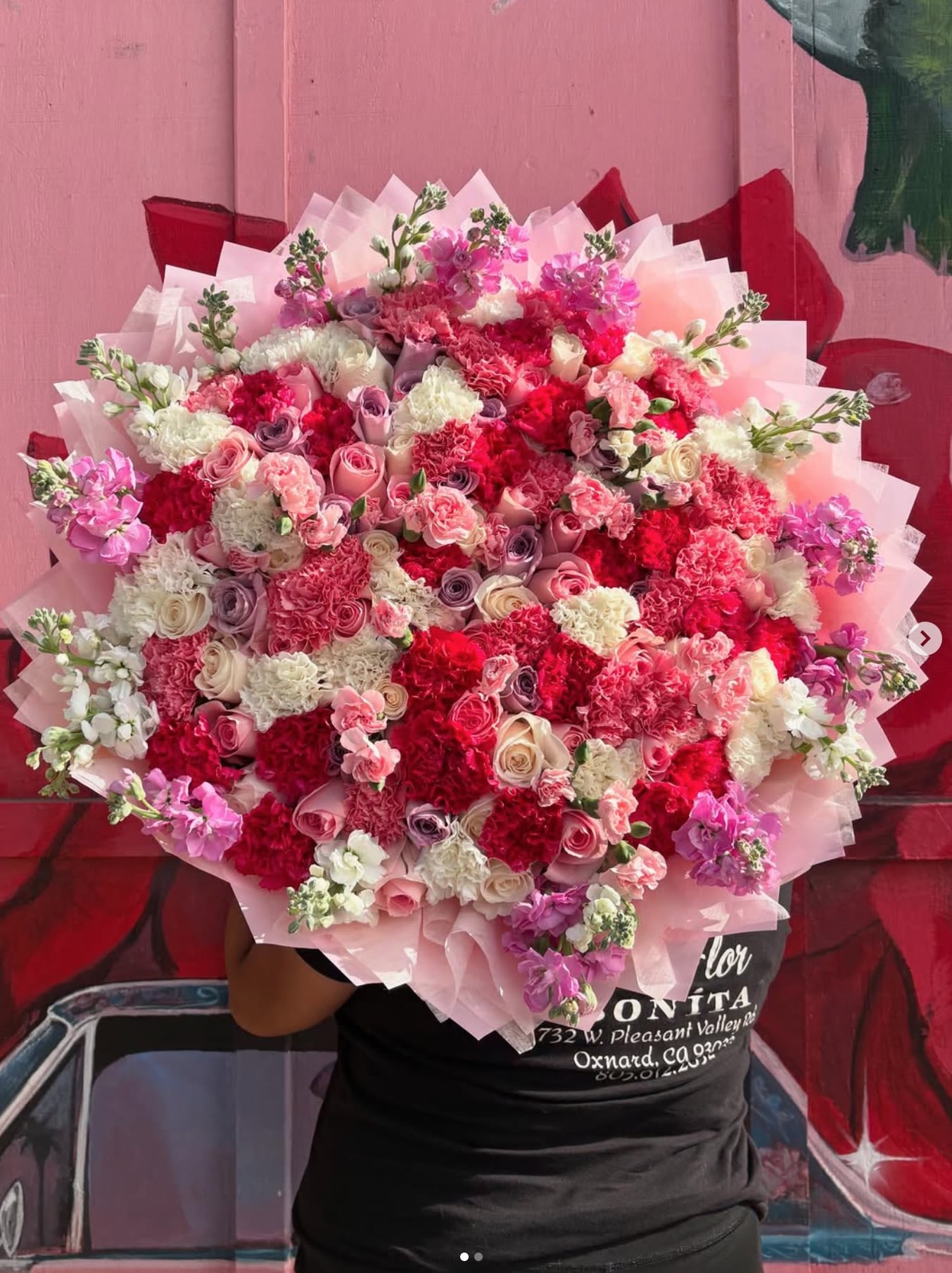 Large bouquet of pink, red, and white flowers wrapped in pale pink paper