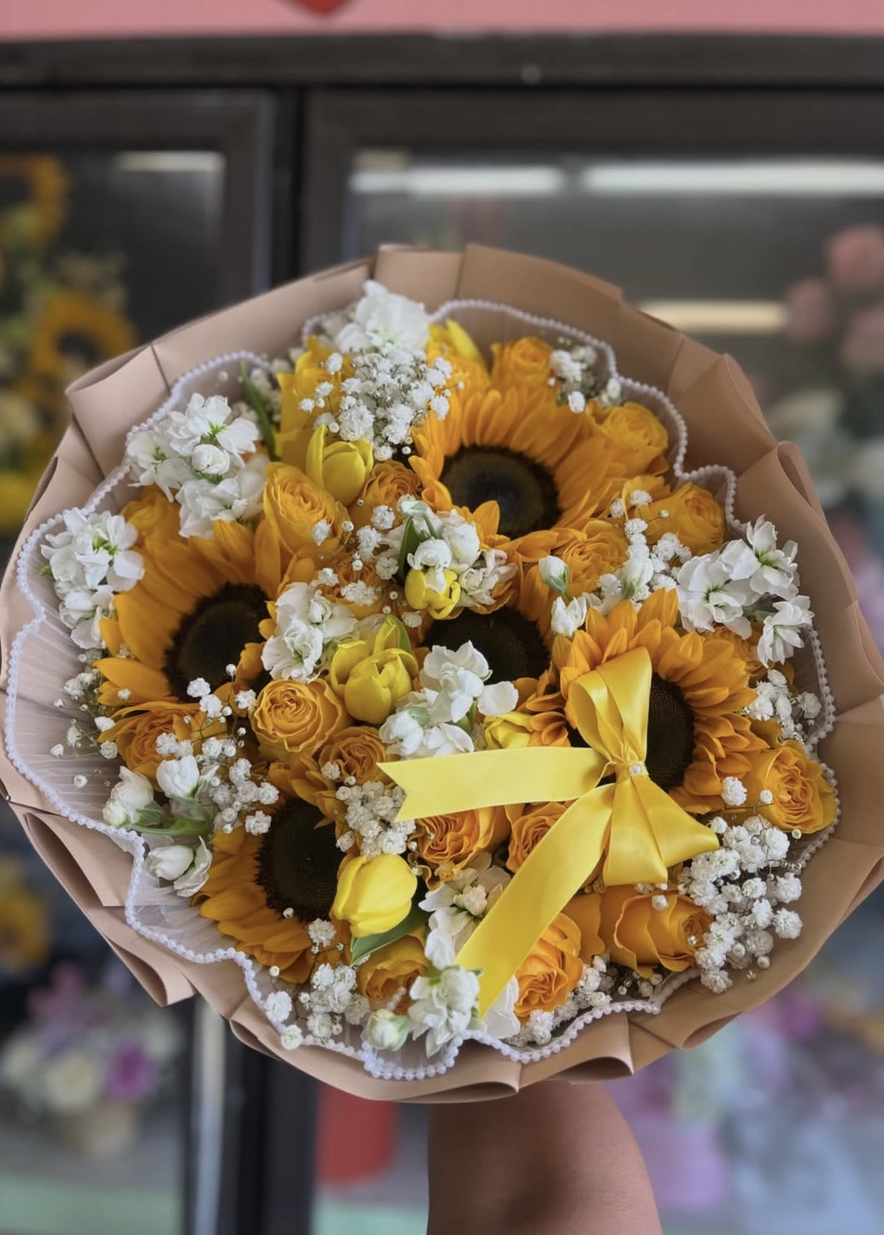 Bouquet of sunflowers, yellow roses, and white filler flowers with a yellow ribbon