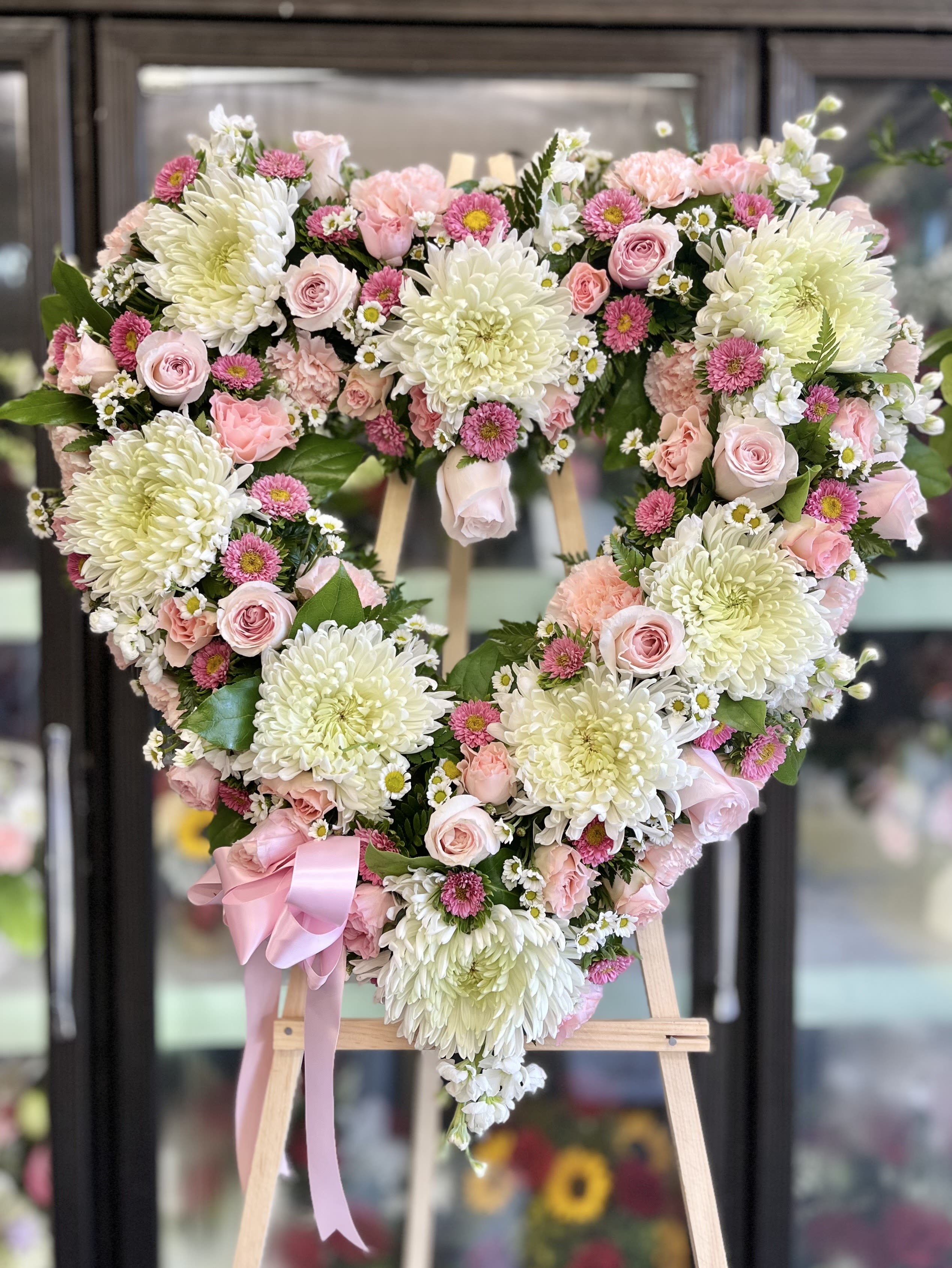 Heart-shaped floral wreath with pink and white flowers on an easel