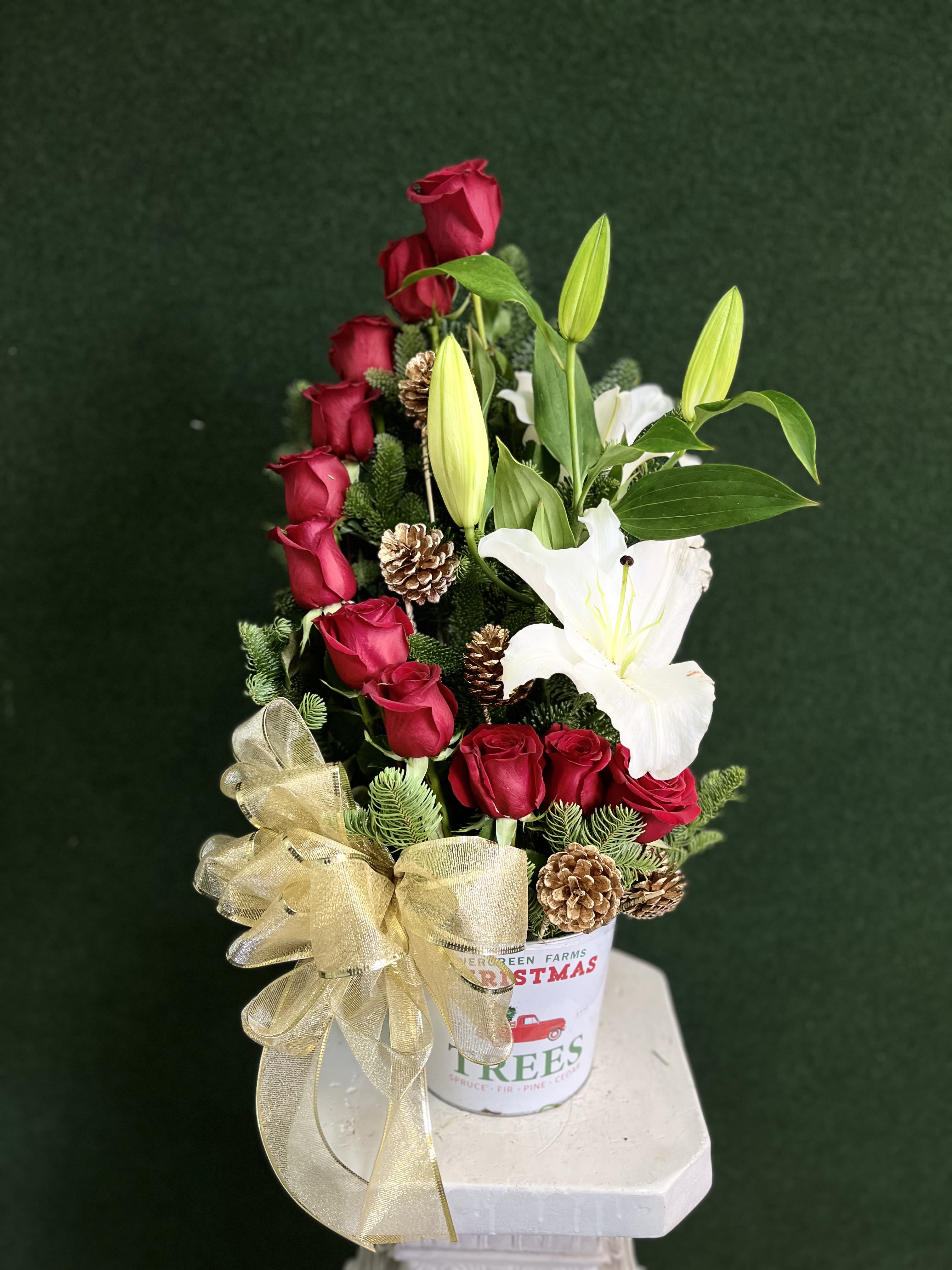 Red roses and white lilies in a festive holiday container with a gold bow