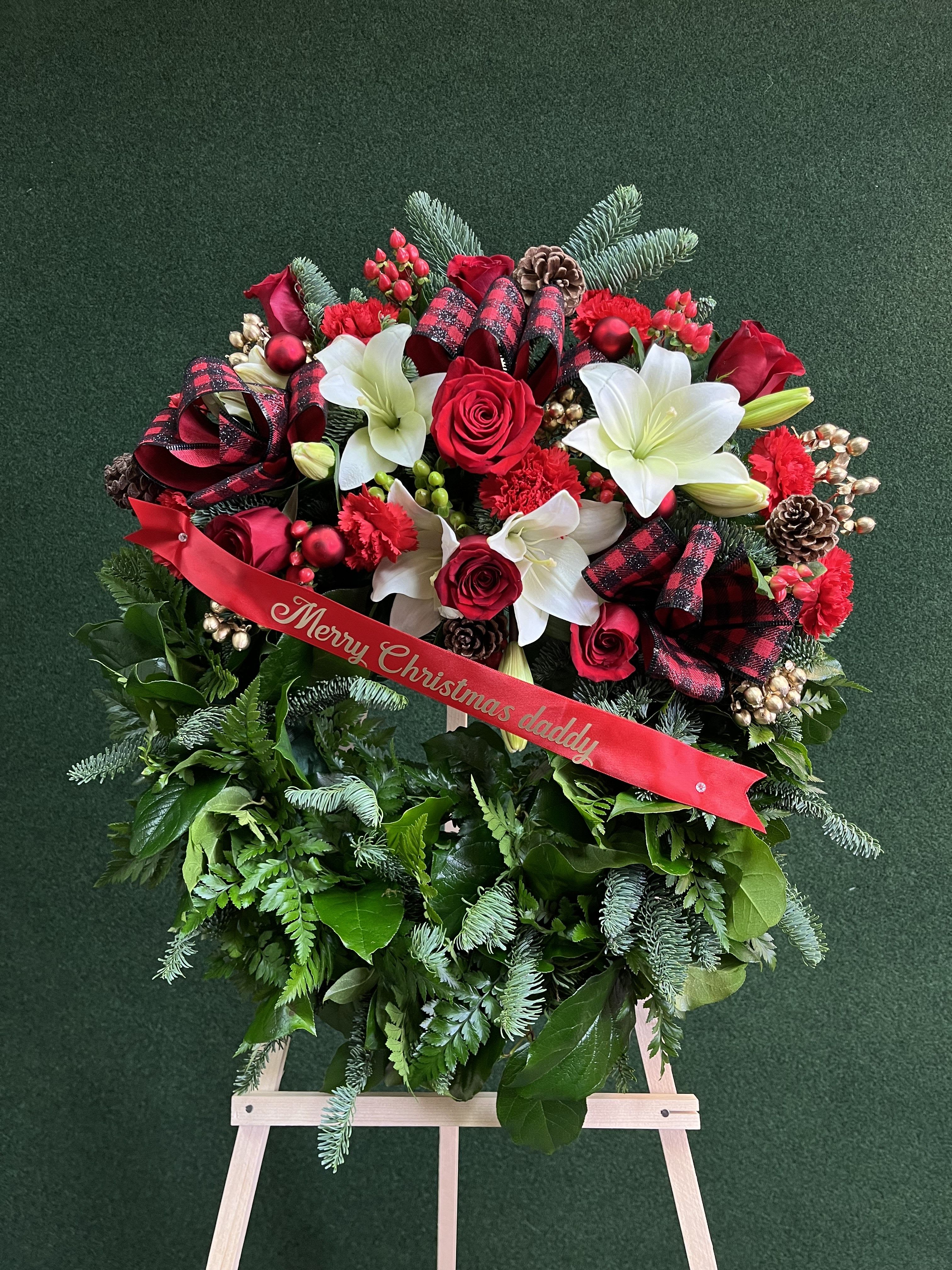 Christmas floral wreath with red roses, white lilies, and a ribbon on an easel
