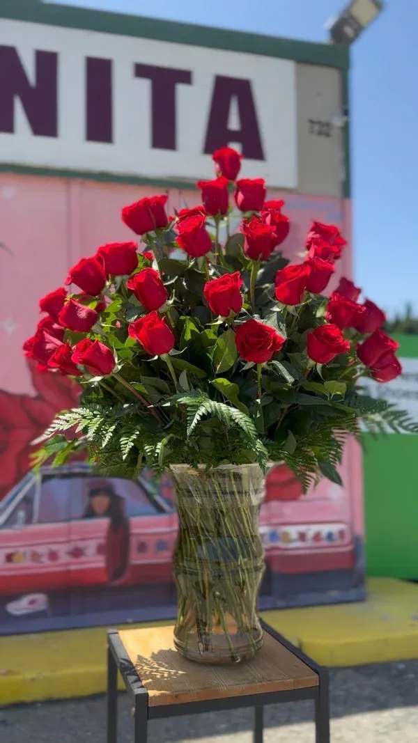 Tall vase arrangement of red roses with fern foliage