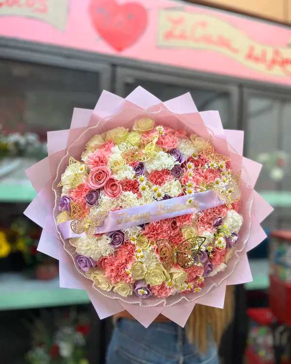 Large pastel bouquet of roses, carnations, and small daisies wrapped in pink paper